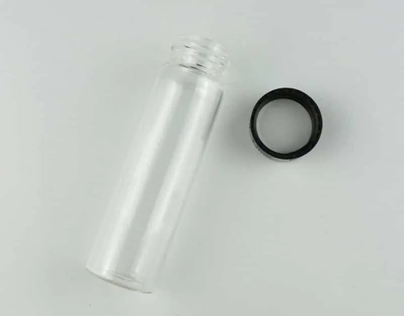 A Clear Borosilicate Reagent Lab Glass bottle 50ml from the 10pcs set is shown lying next to a black screw cap on a white surface.