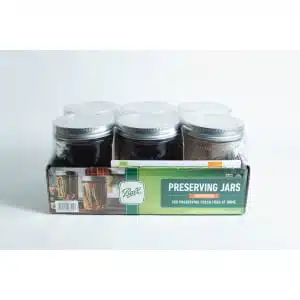 A set of six Ball Mason pint jars with wide mouths are organised in a cardboard box labelled "Preserving Jars" and shown against a white background.