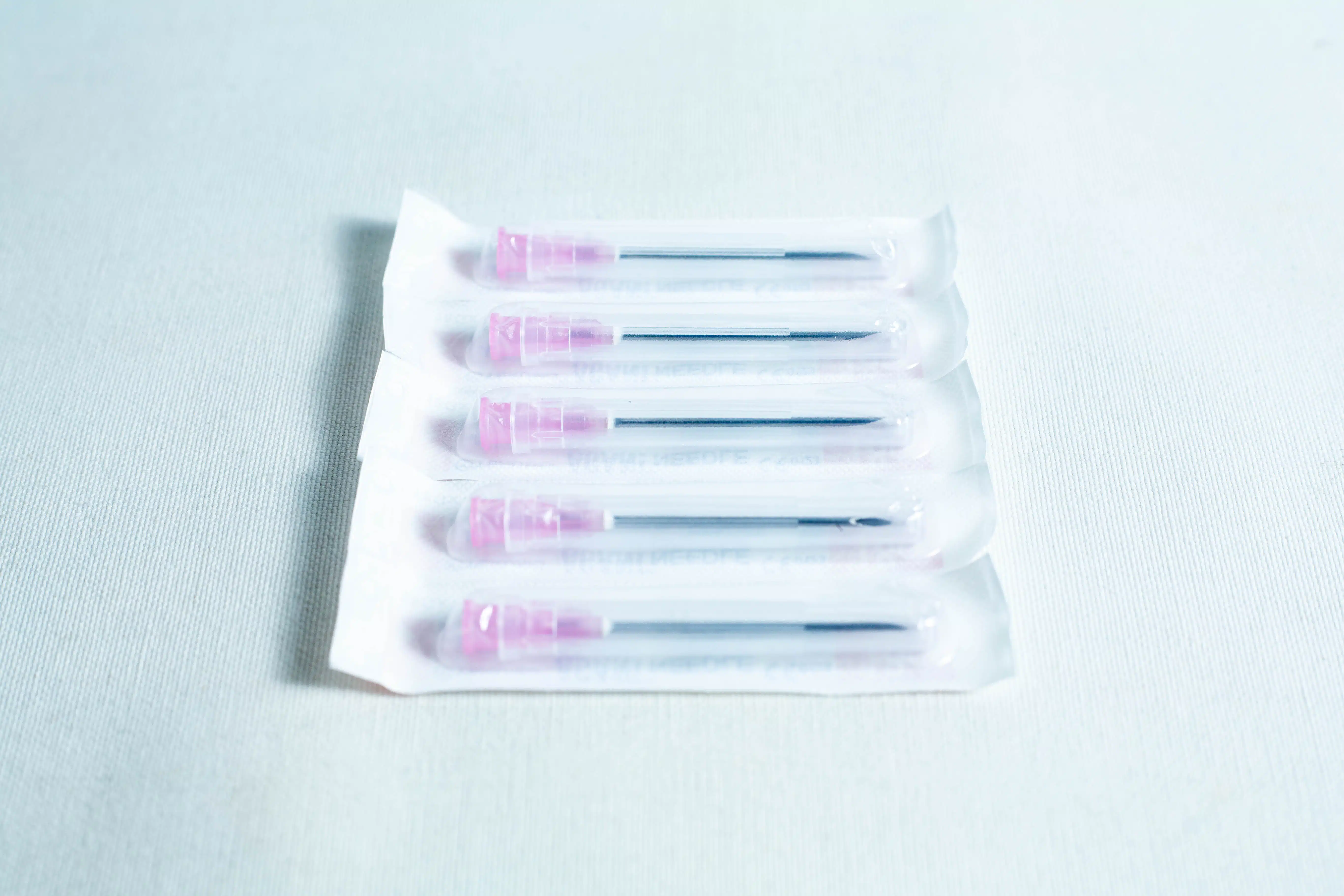 A box of 100 sterile 18G hypodermic needles, each with a pink cap and individually wrapped, is displayed on a white surface.