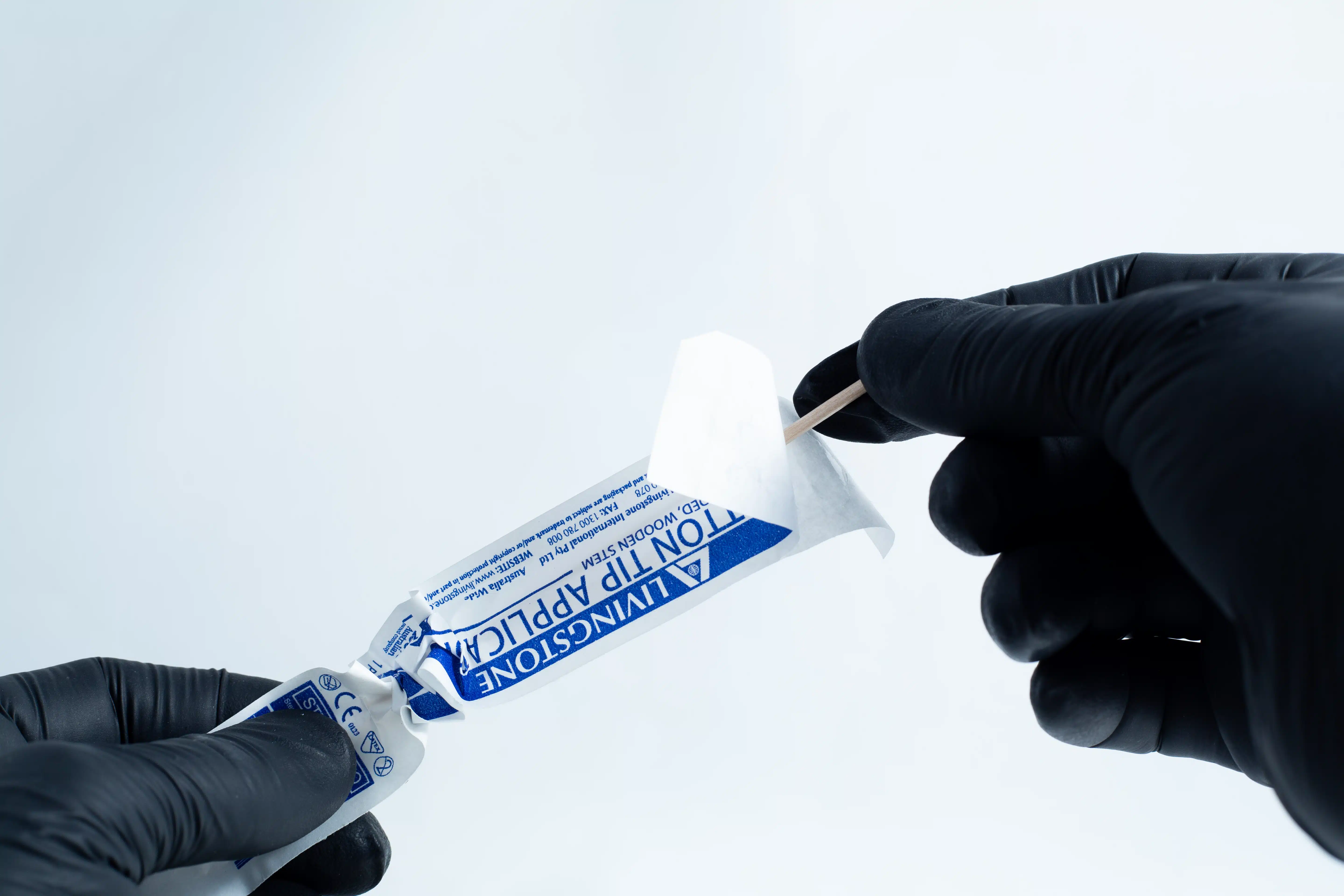 Gloved hands opening a blue antiseptic towelette packet with a cotton bud and the Agar petri dish MEA School Science Fun Project Kit nearby, set on a white background—ideal for school science experiments.