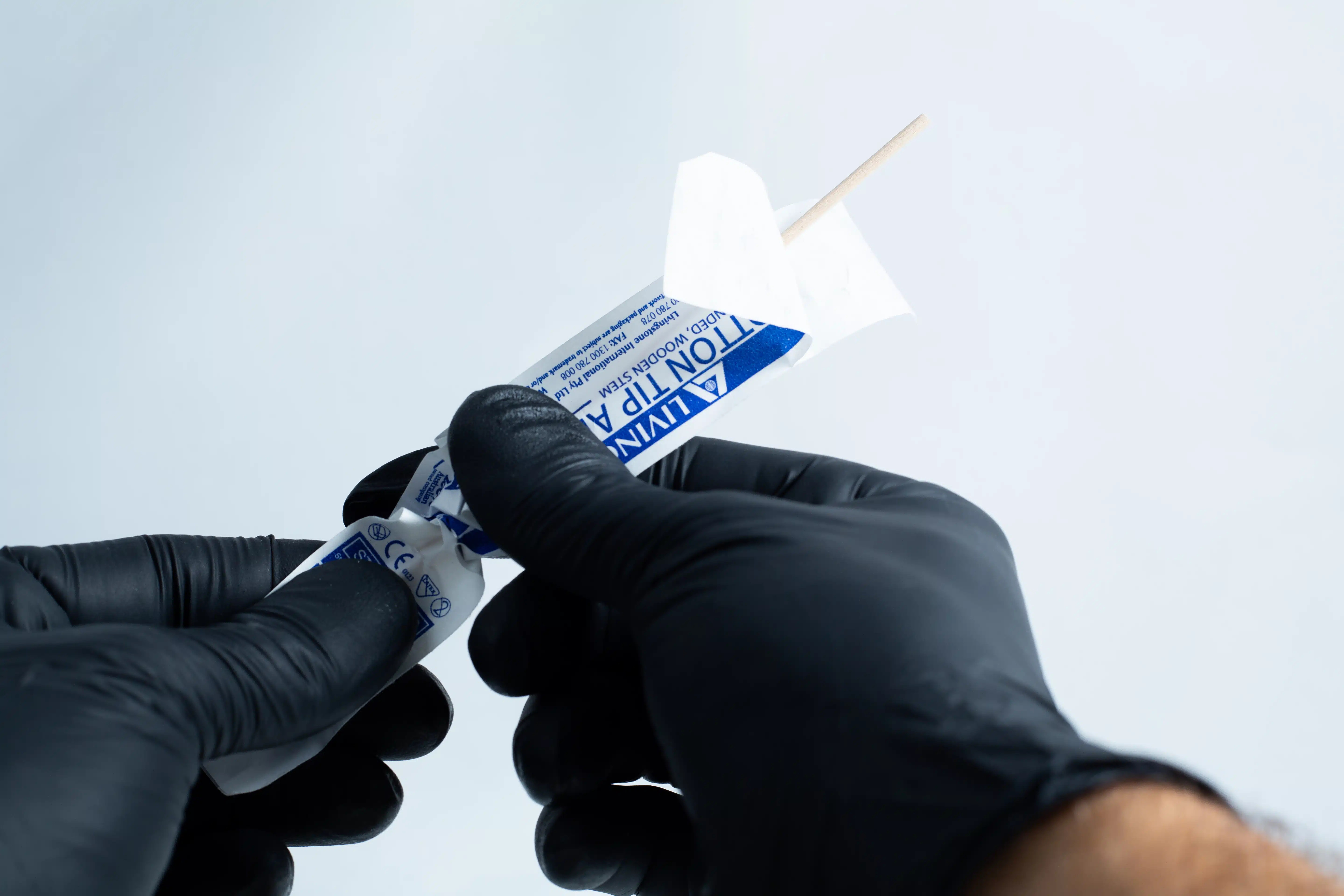Gloved hands open a sterile wooden tongue depressor from its packaging, ready to use with the Agar petri dish MEA School Science Fun Project Kit for school experiments.