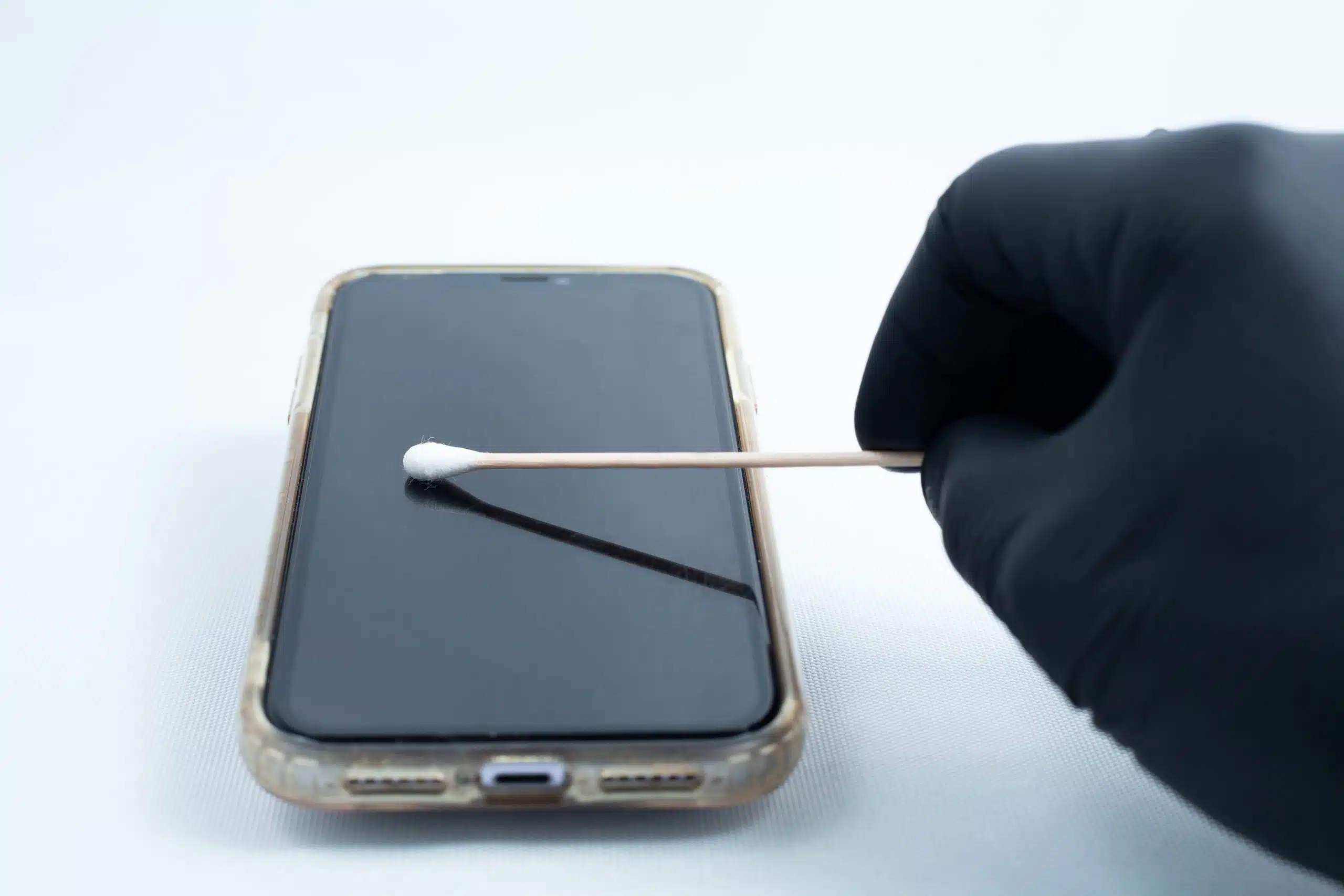 A gloved hand cleans a smartphone screen with a cotton bud, resembling the precise care used in school science projects with the Agar petri dish MEA School Science Fun Project Kit.
