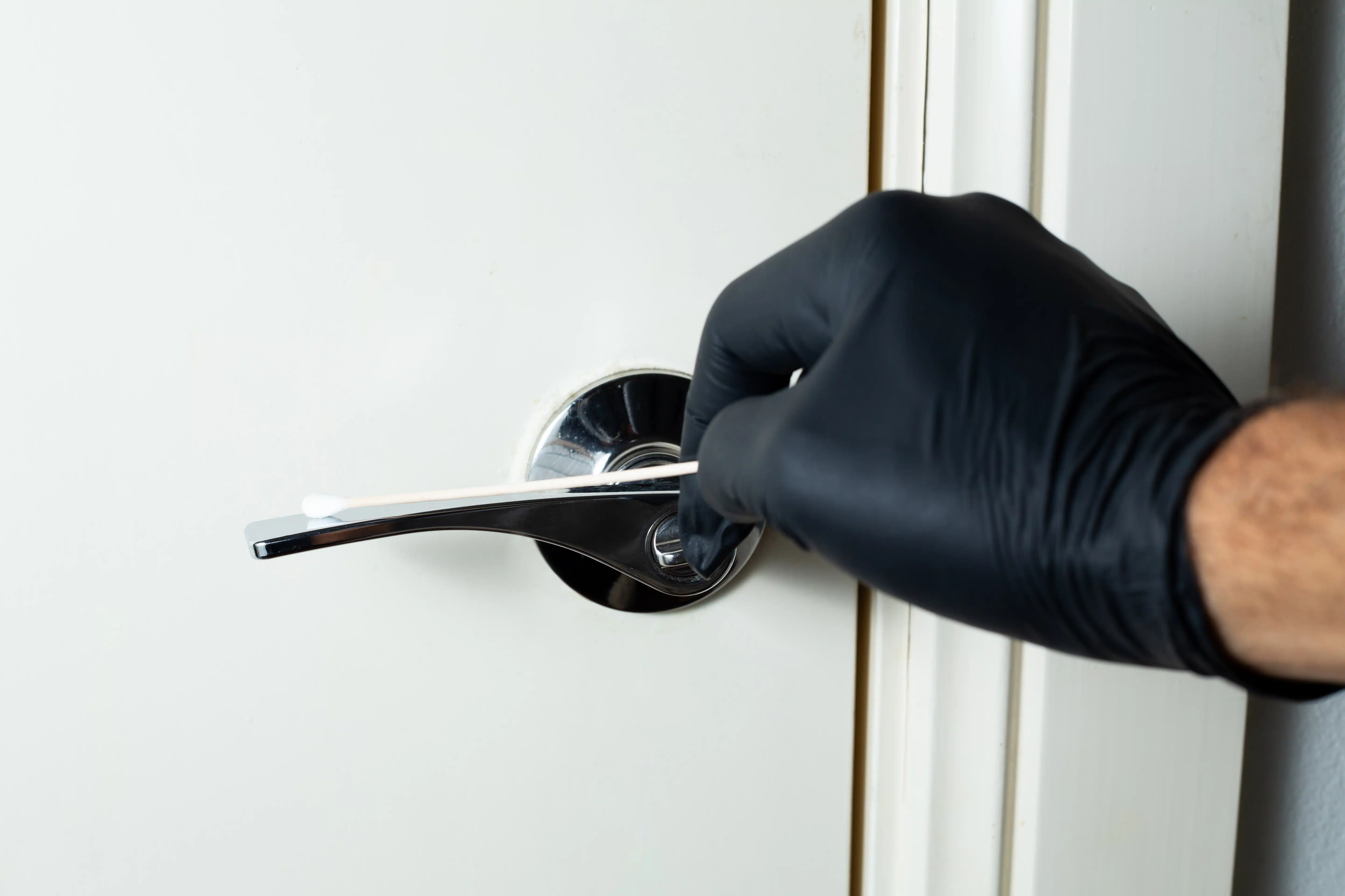 A gloved hand holds a cotton bud near a door handle, likely collecting evidence for a school experiment using the Agar Petri dish MEA School Science Fun Project Kit.