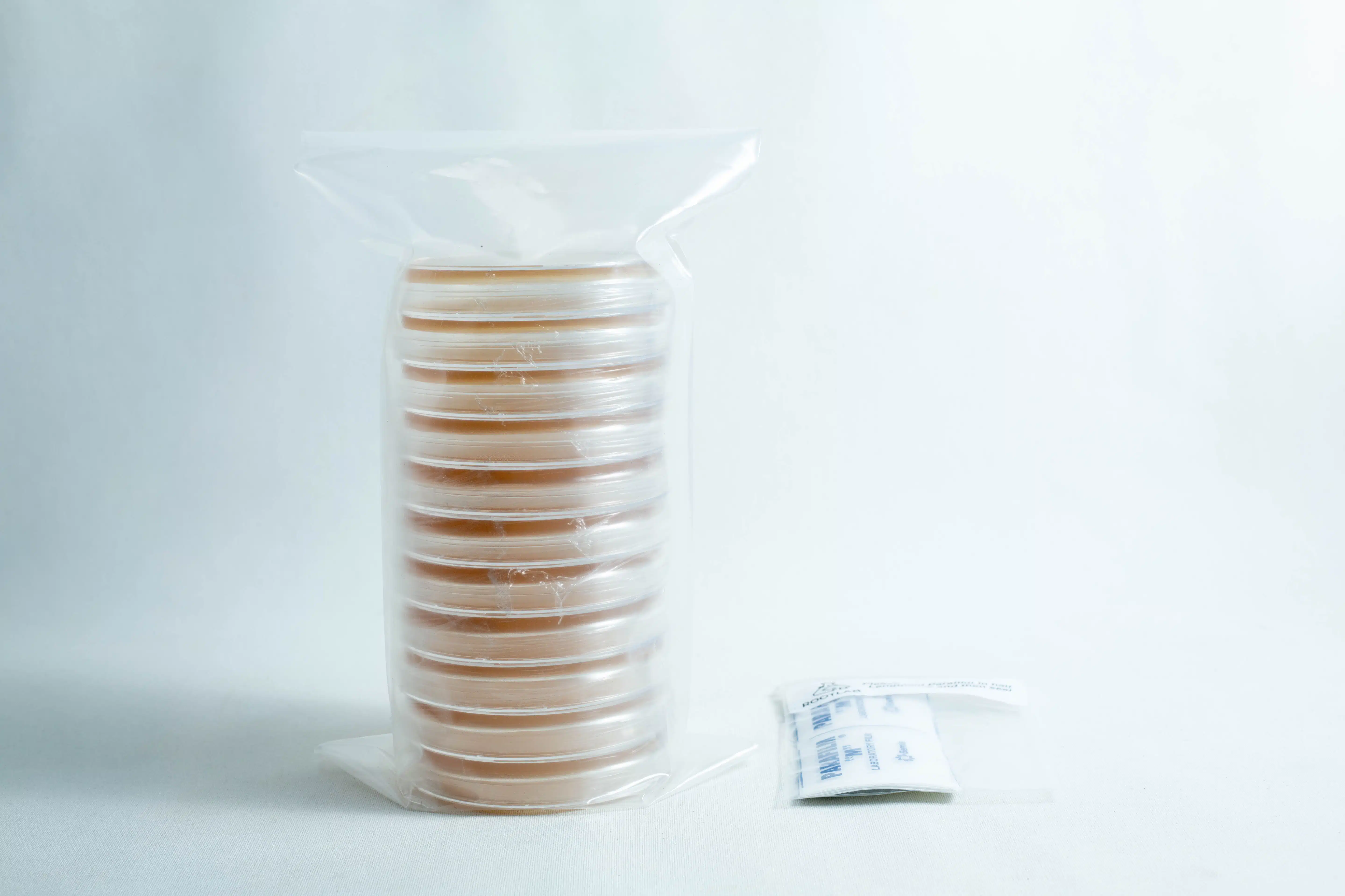 Pre poured MEAG Agar Plates (Antibacterial) 90mm 1 A stack of pre-poured MEAG agar plates (antibacterial) 90mm, sealed in plastic, sits next to a small packet on a white surface.