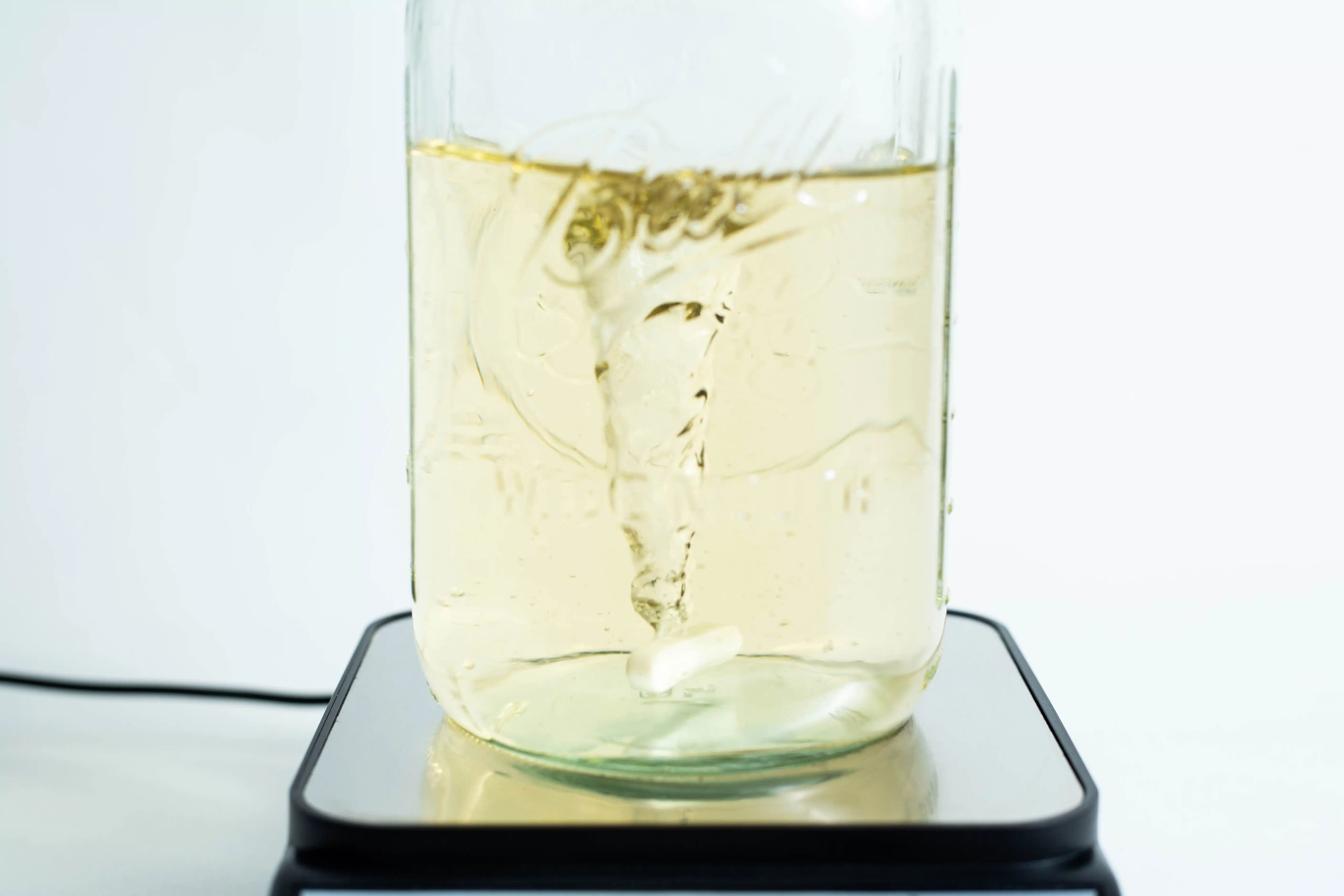 Magnetic Stirrer machine 3500rpm 5 A vortex swirls in a yellow liquid within a glass jar on the Magnetic Stirrer Ciblanc 3500rpm, highlighting the stirring precision of this device.