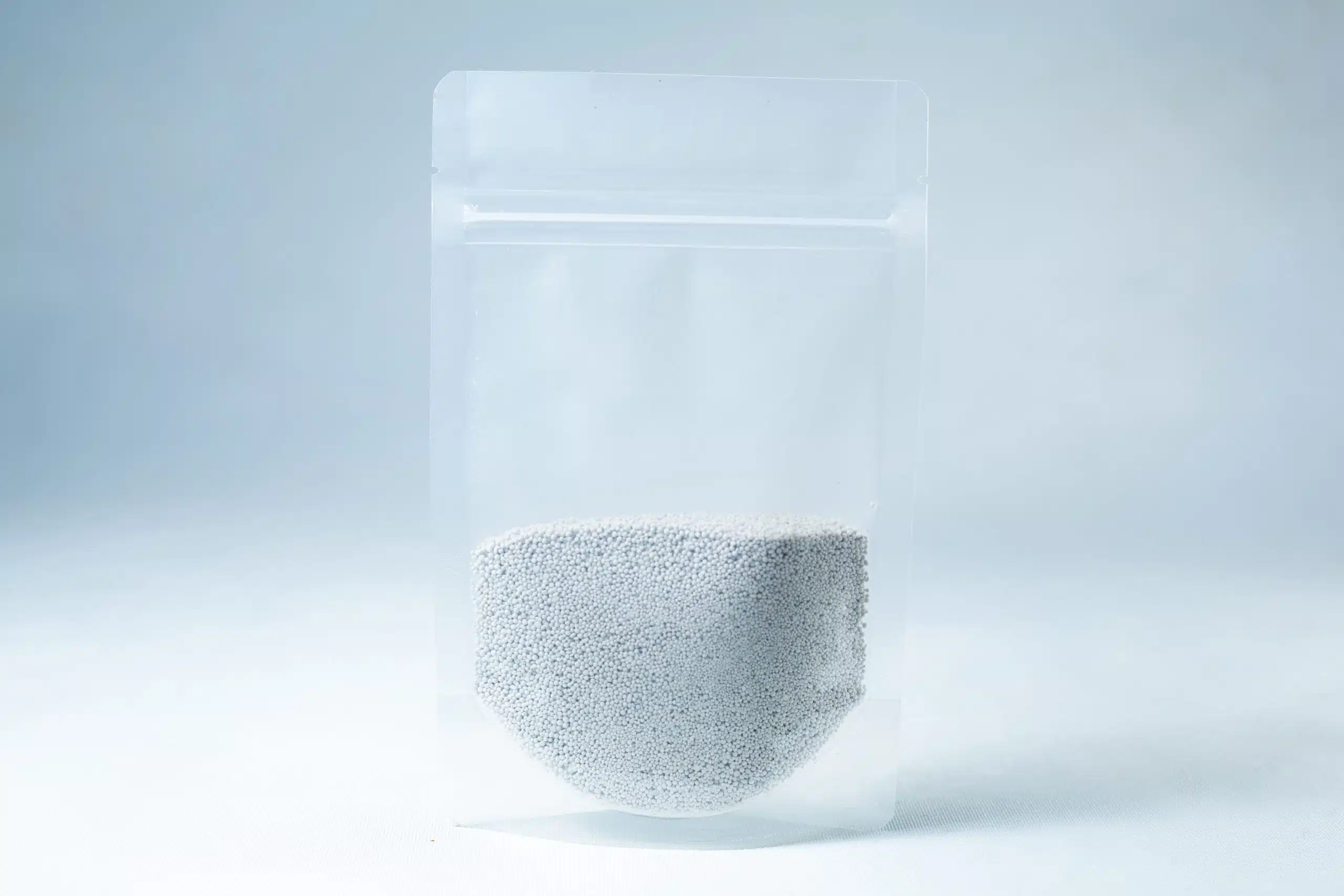 A clear resealable plastic pouch filled halfway with Natural Gypsum coarse grade mushroom supplement grain and substrate, featuring small white gypsum granules, shown on a light background.