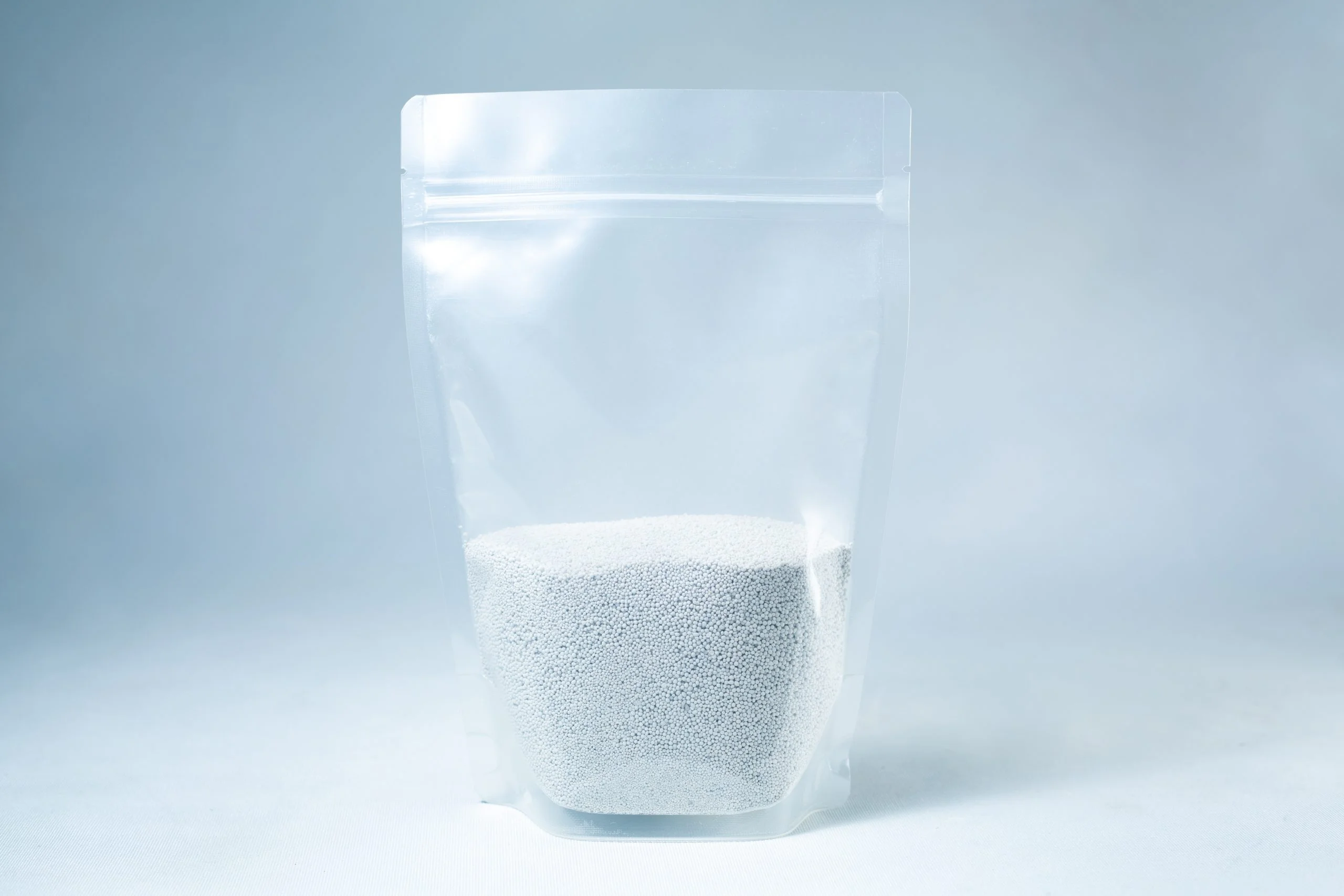 A clear resealable pouch containing white coarse Natural Gypsum mushroom supplement grain and substrate stands on a light background—perfect for storage and use.