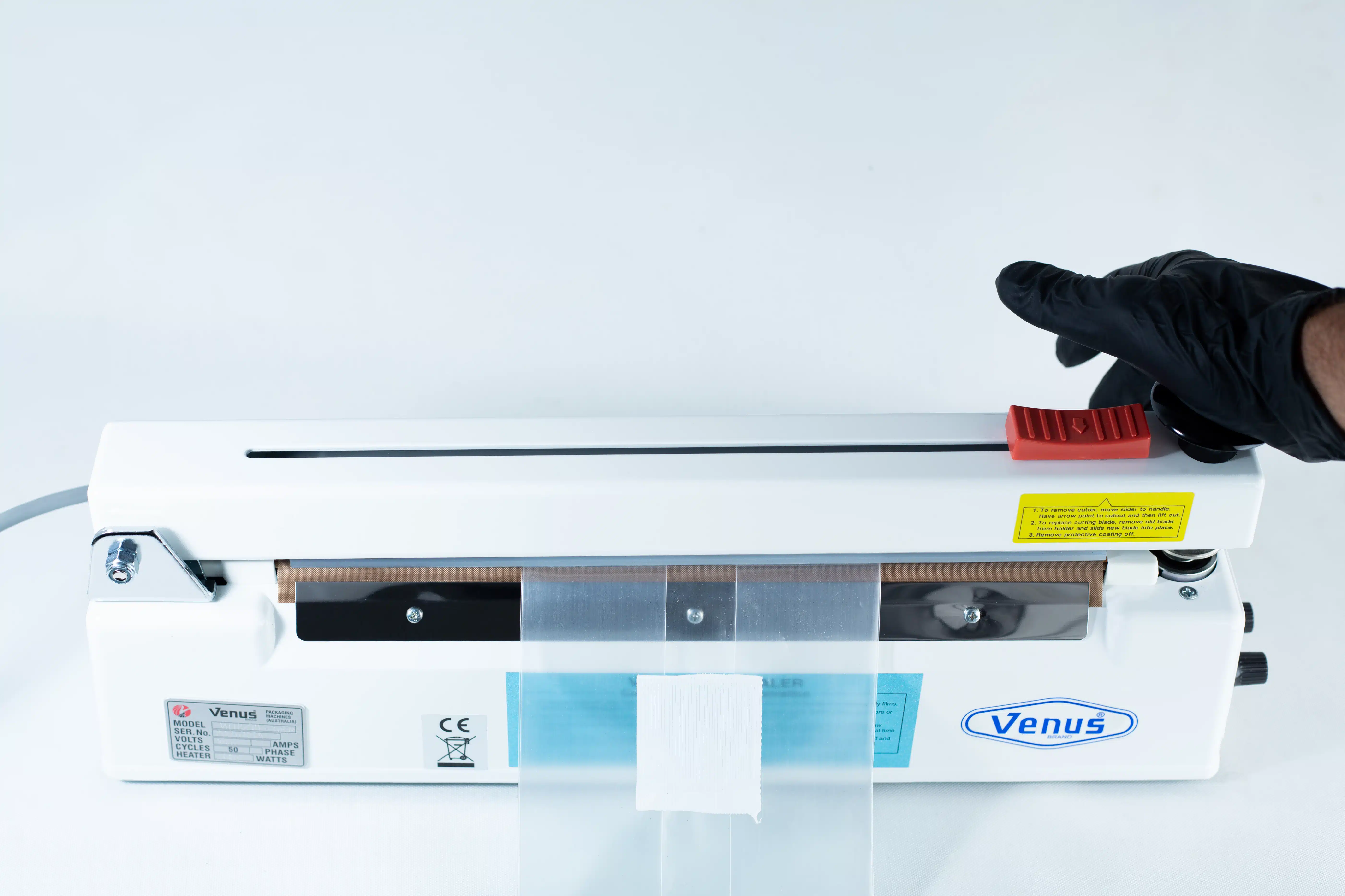 Heat Sealer 30cm Seal Width 5mm with cutter and Magnet 5 A gloved hand operates a Heat Sealer 30cm Seal Width 5mm with cutter and magnet, sealing a plastic bag securely inside the machine.