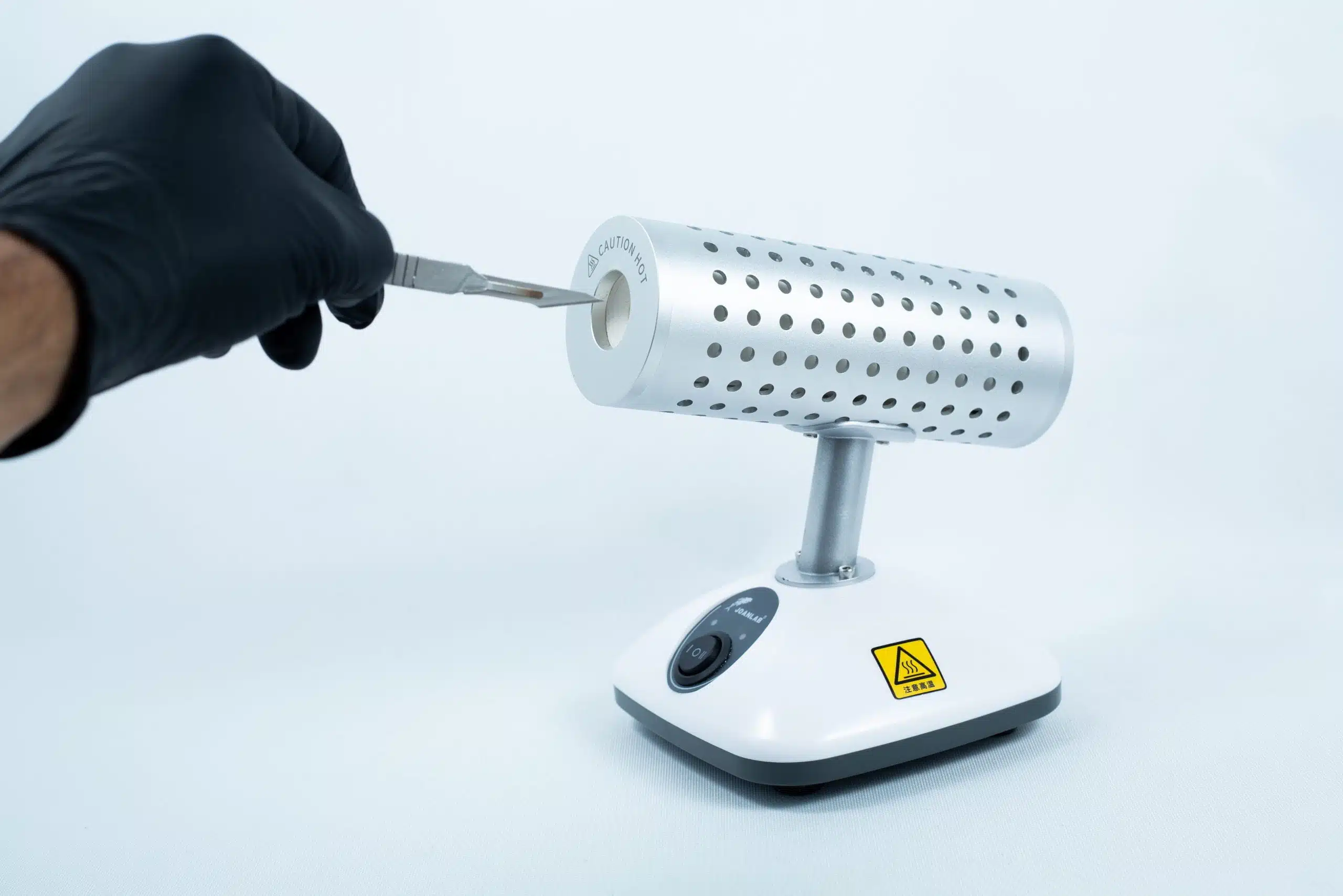 A gloved hand inserts a tool into the Infrared Steriliser Bacti Cinerator Lab tool, which features a warning sign on its base, in the laboratory.
