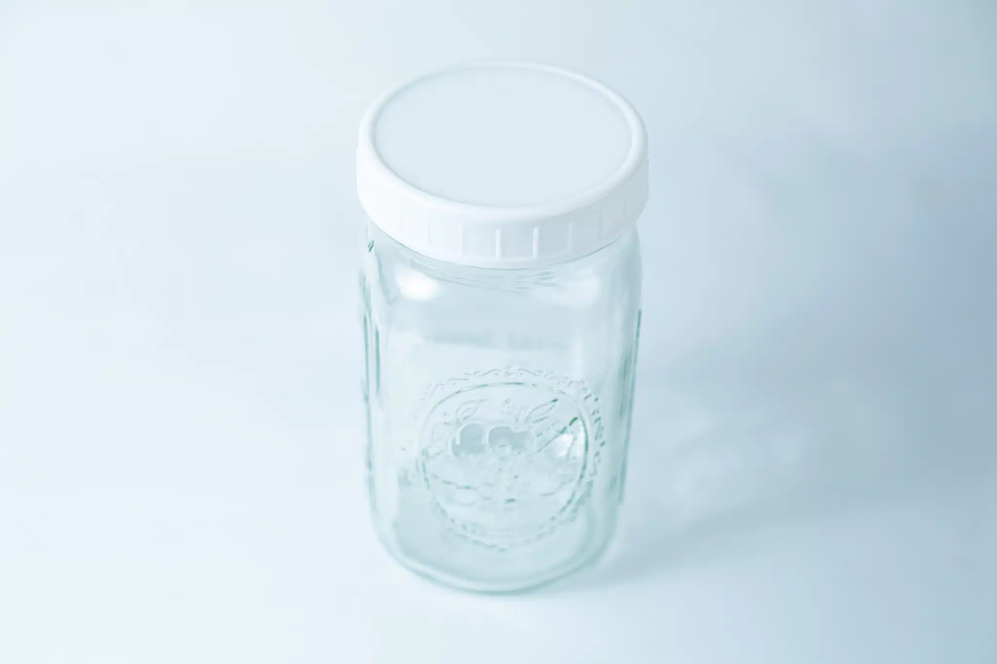 Mason Jar Lids | Wide mouth 86mm | Plain White Plastic Lids 6 Photographed on a light blue background, this clear glass jar features a plain white plastic lid, designed to fit wide mouth mason jars with 86mm Mason Jar Lids | Wide Mouth | Plain White Plastic Lids.