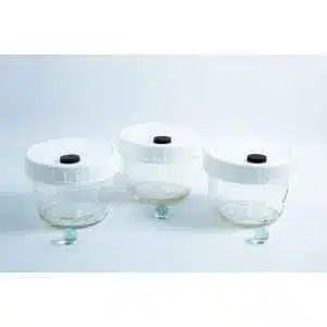 Three empty Mycology Ball Mason jars (1L, genuine, autoclavable) with injection port and air vent, each with a white lid and placed in front of a small green marble, arranged on a white background.