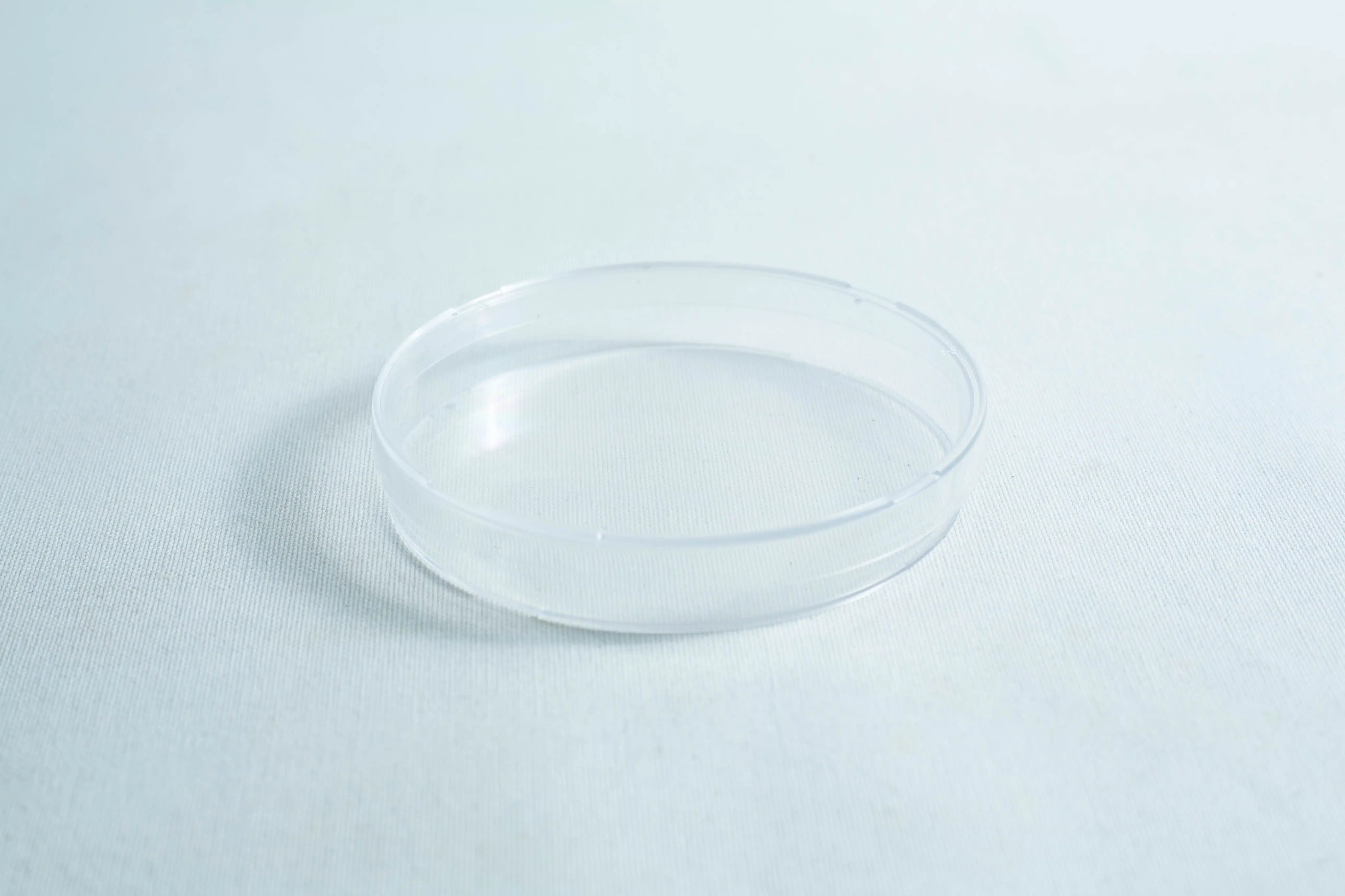 A clear, sterile 90mm Petri dish with 3 vents, gamma irradiated for laboratory use, sits empty on a white surface, highlighting its simplicity.