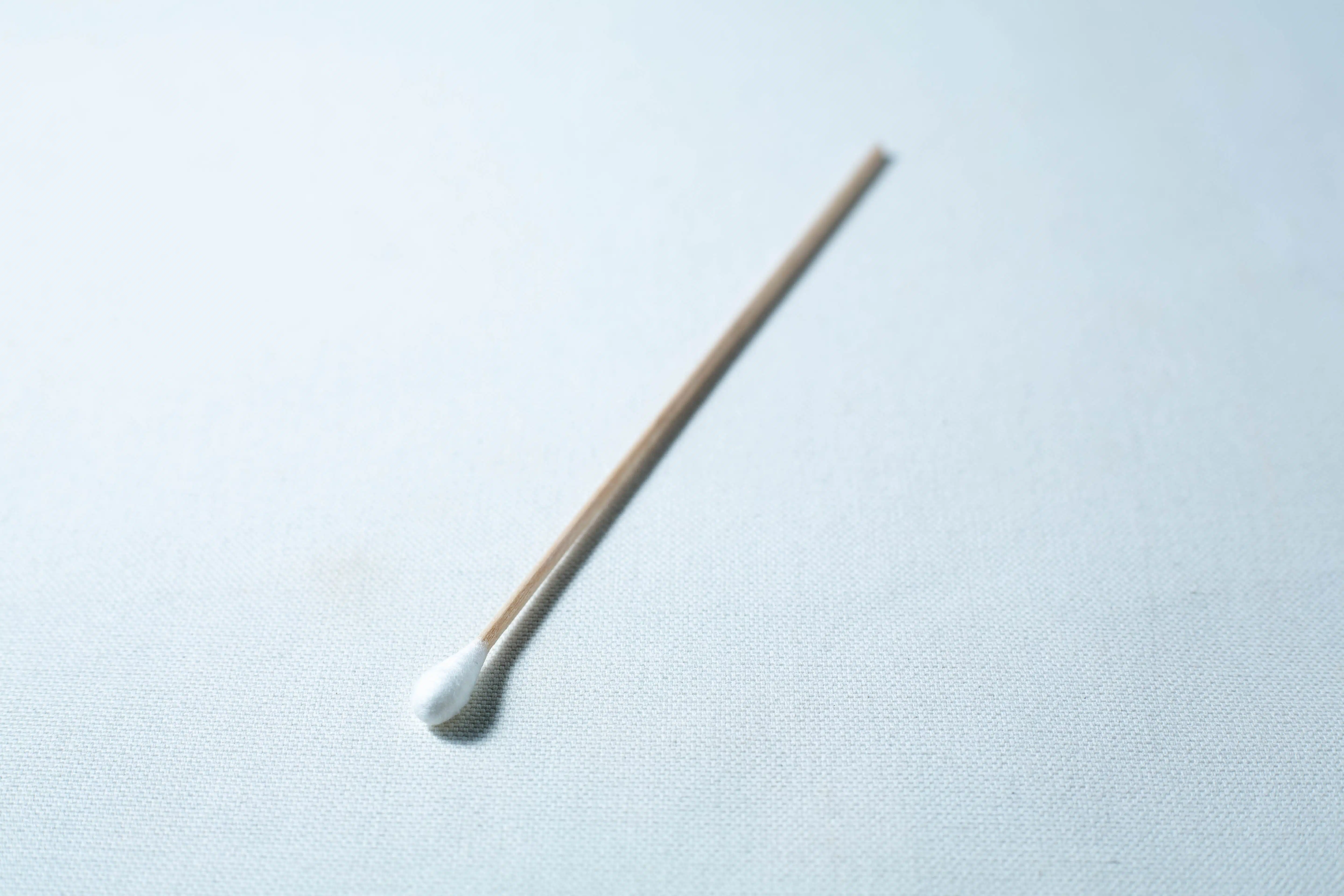 A single sterile cotton wool bud with a wooden stick is placed on a white surface.
