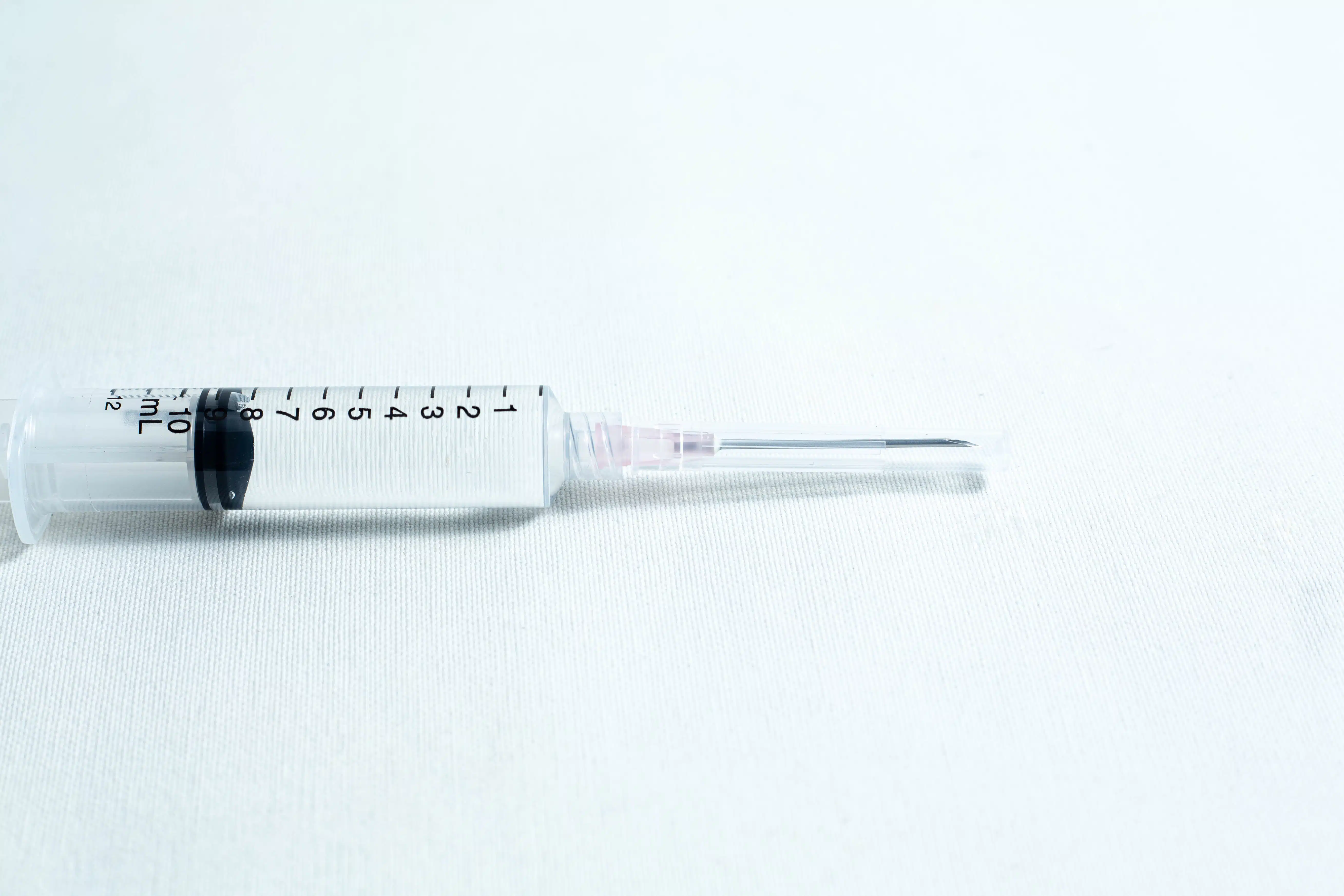 A syringe with clear liquid rests on a white surface, fitted with a sterile 18G hypodermic needle from a box of 100pcs.