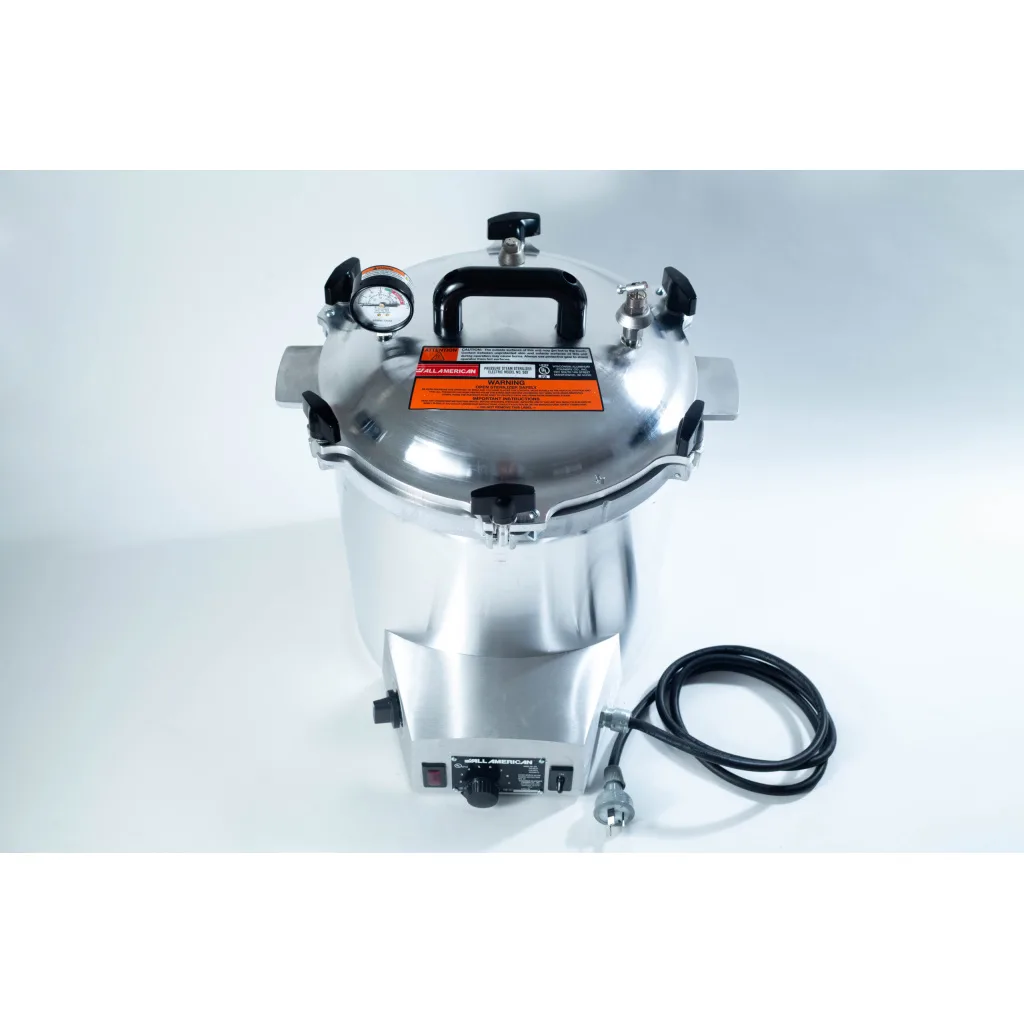 A stainless steel pressure cooker with a gauge, black handles, and an attached power lead on a white background.