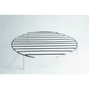 Round metal grill rack with three legs, standing on a white surface, photographed against a plain background.