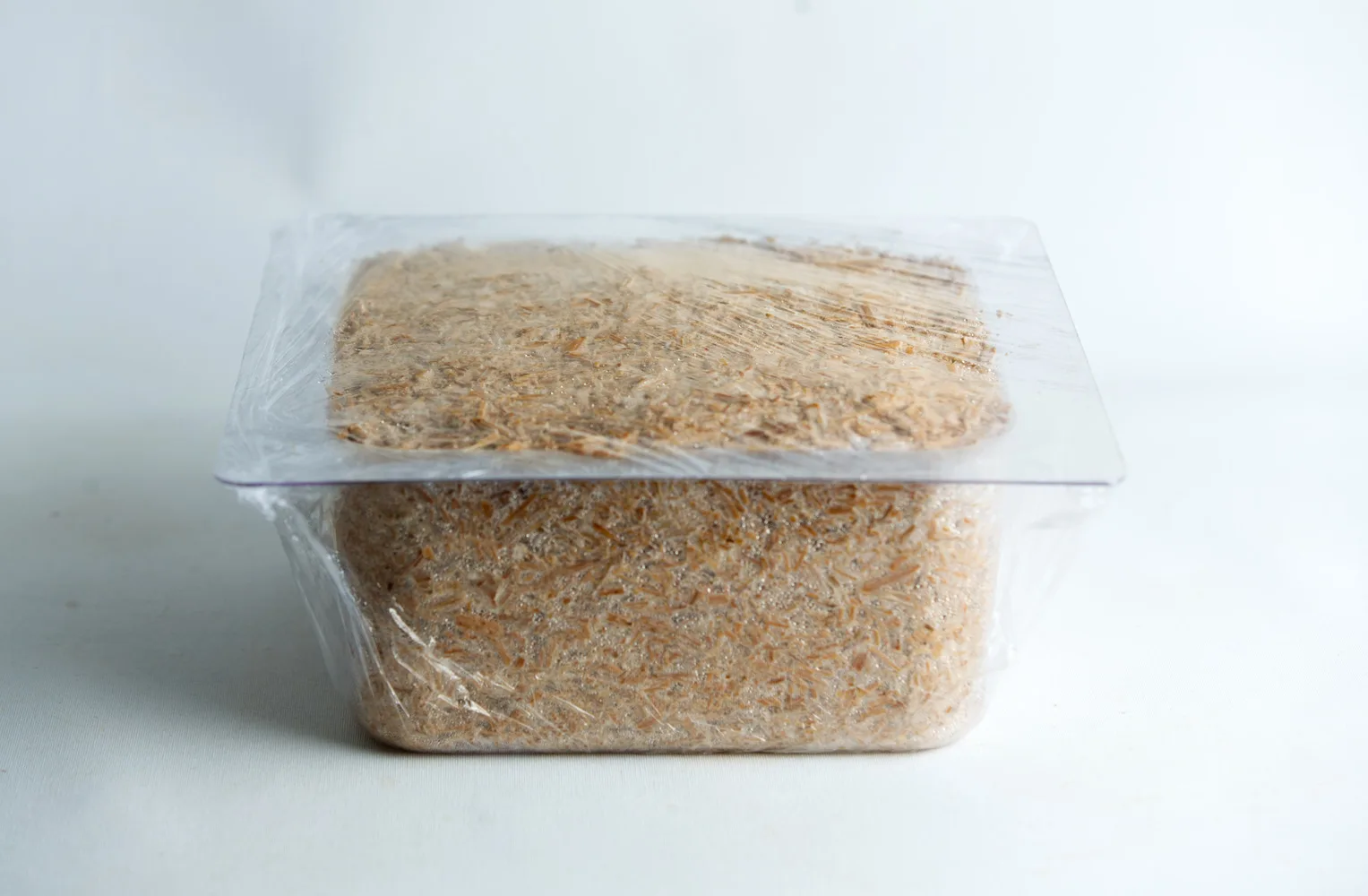 A clear plastic container filled with grated cheese, covered with cling film, on a white background.