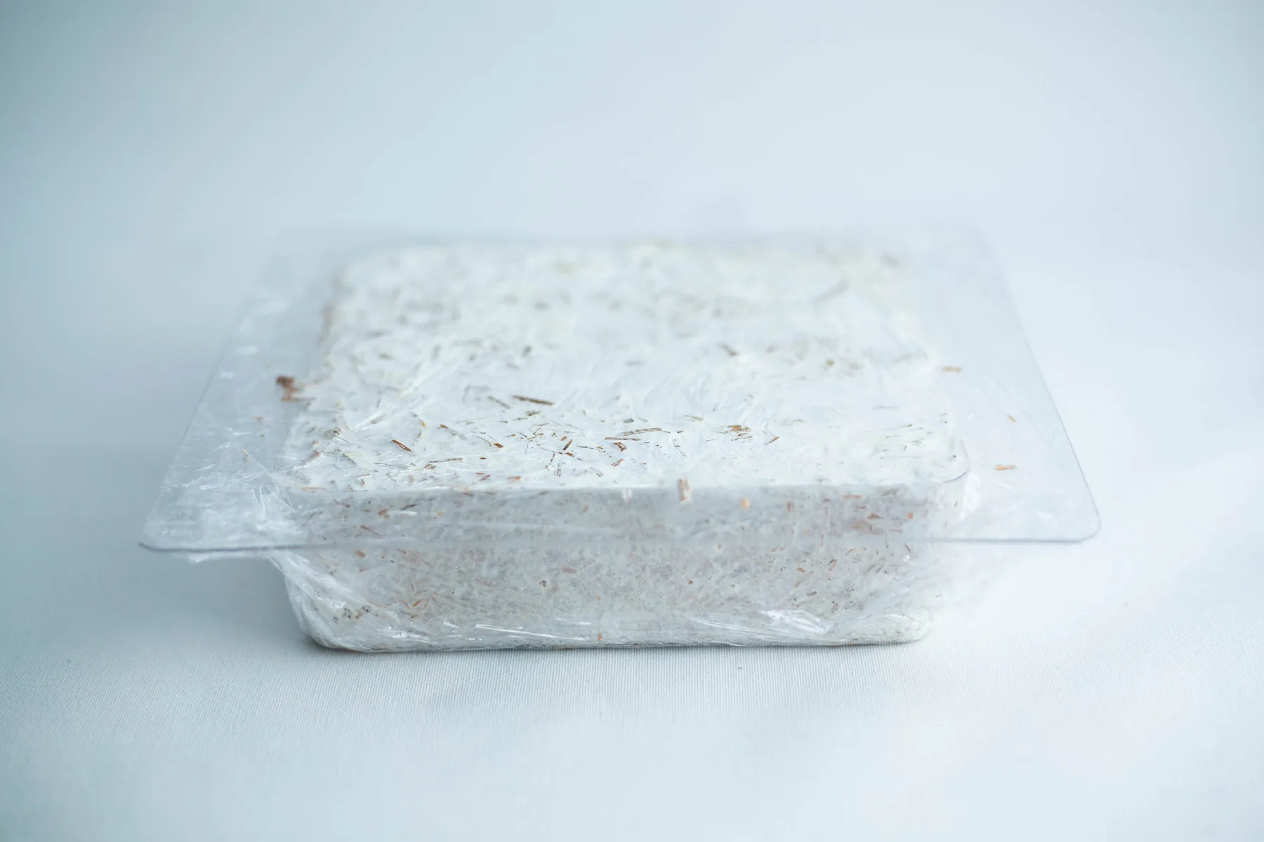 A block of white, shredded material in a clear plastic container on a light background.