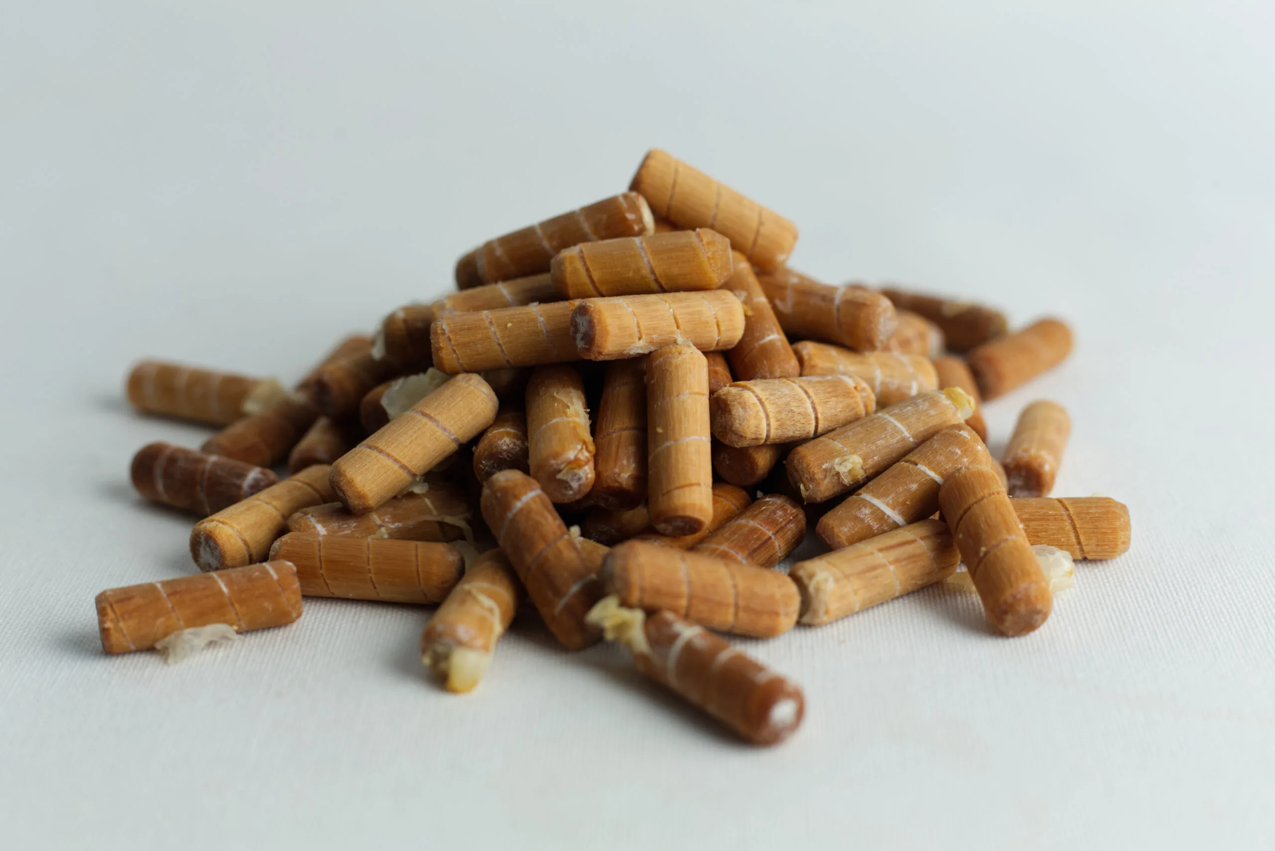 A pile of Log Dowel Mushroom Plug Spawn—Native Australian Reishi (Ganoderma steyaertanum) pellets is shown on a white surface.