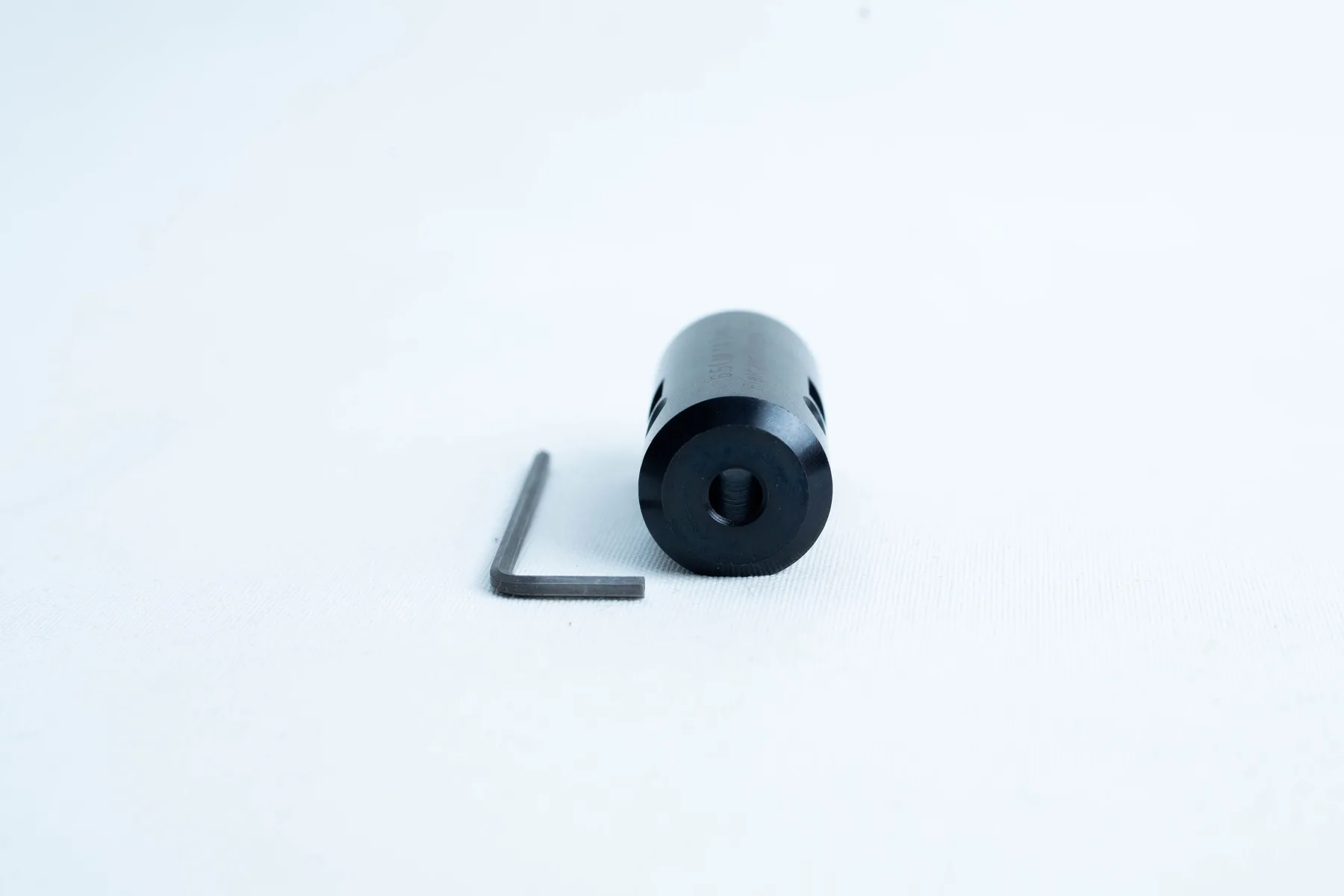A black cylindrical metal part and an L-shaped hex key on a white background.