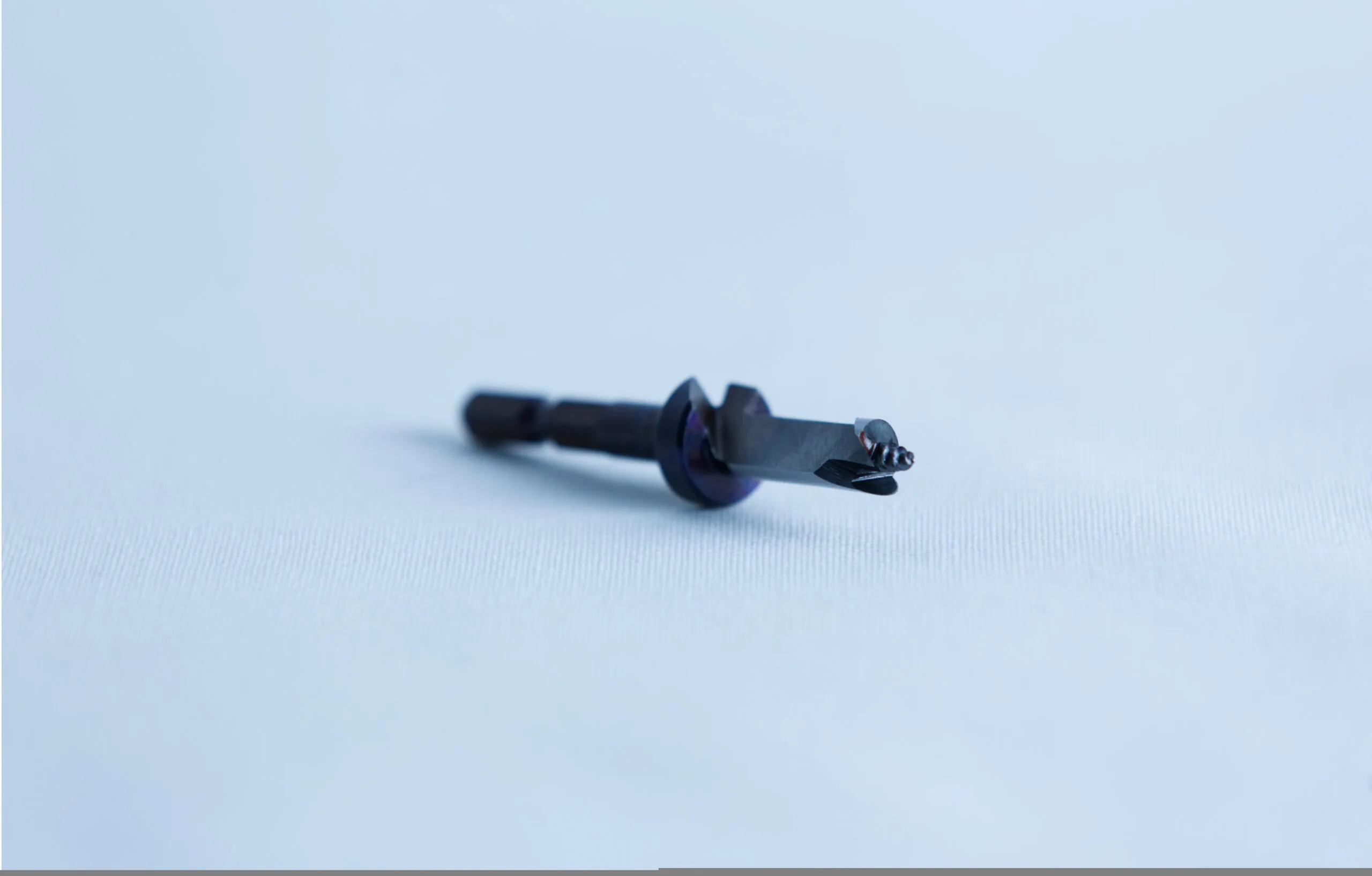 A close-up of a small metal tool or drill bit on a light blue surface with a blurred background.