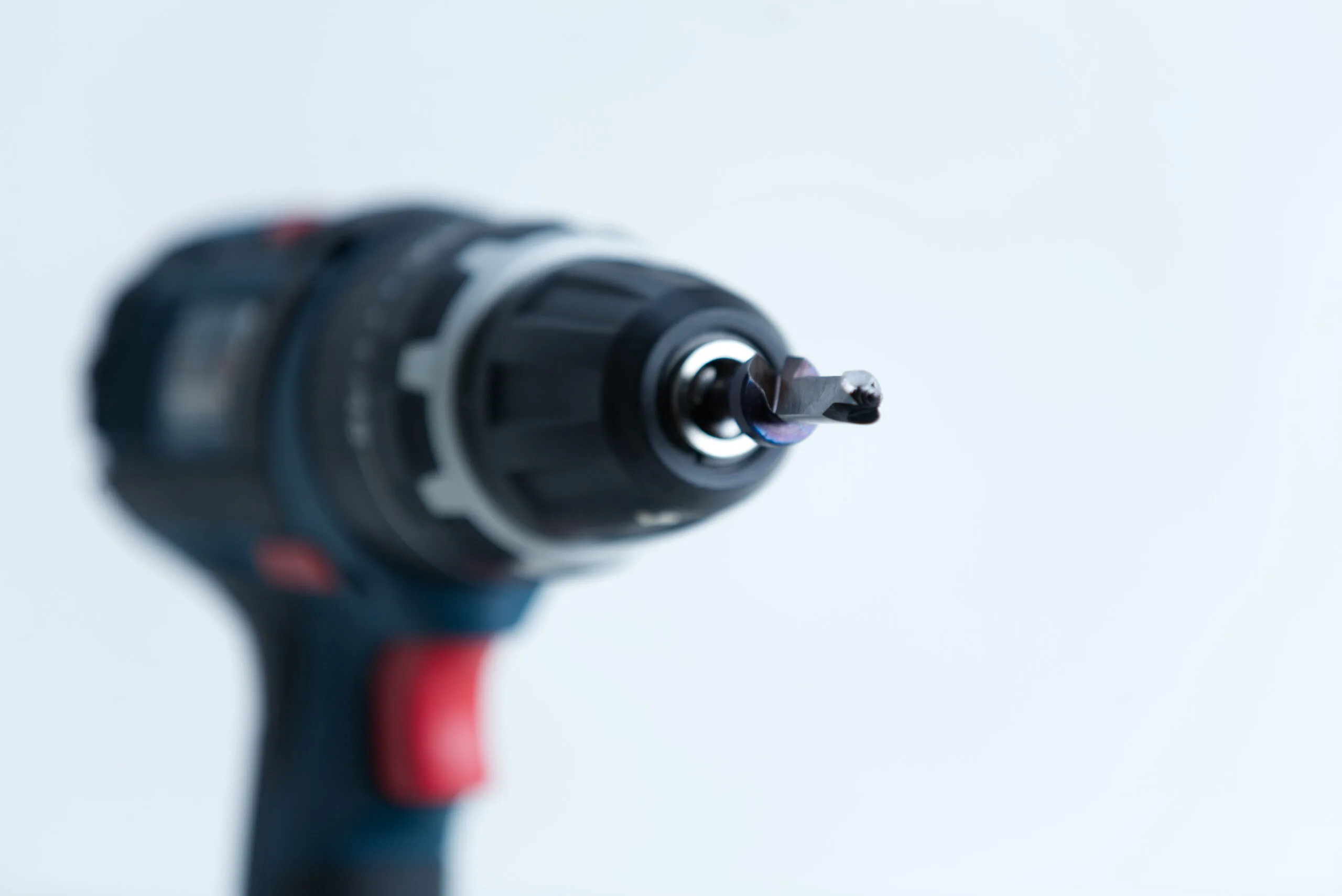 Close-up of a cordless power drill with a screwdriver bit, focussed on the bit against a white background.