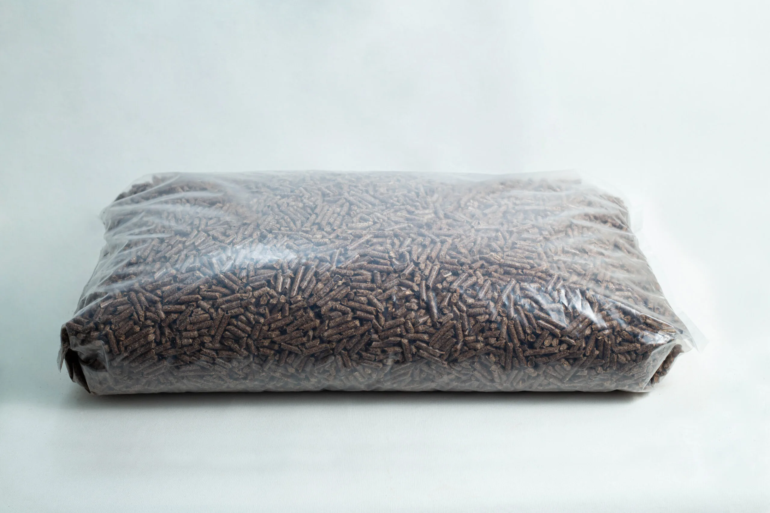 A sealed plastic bag filled with brown wood pellets on a plain white background.