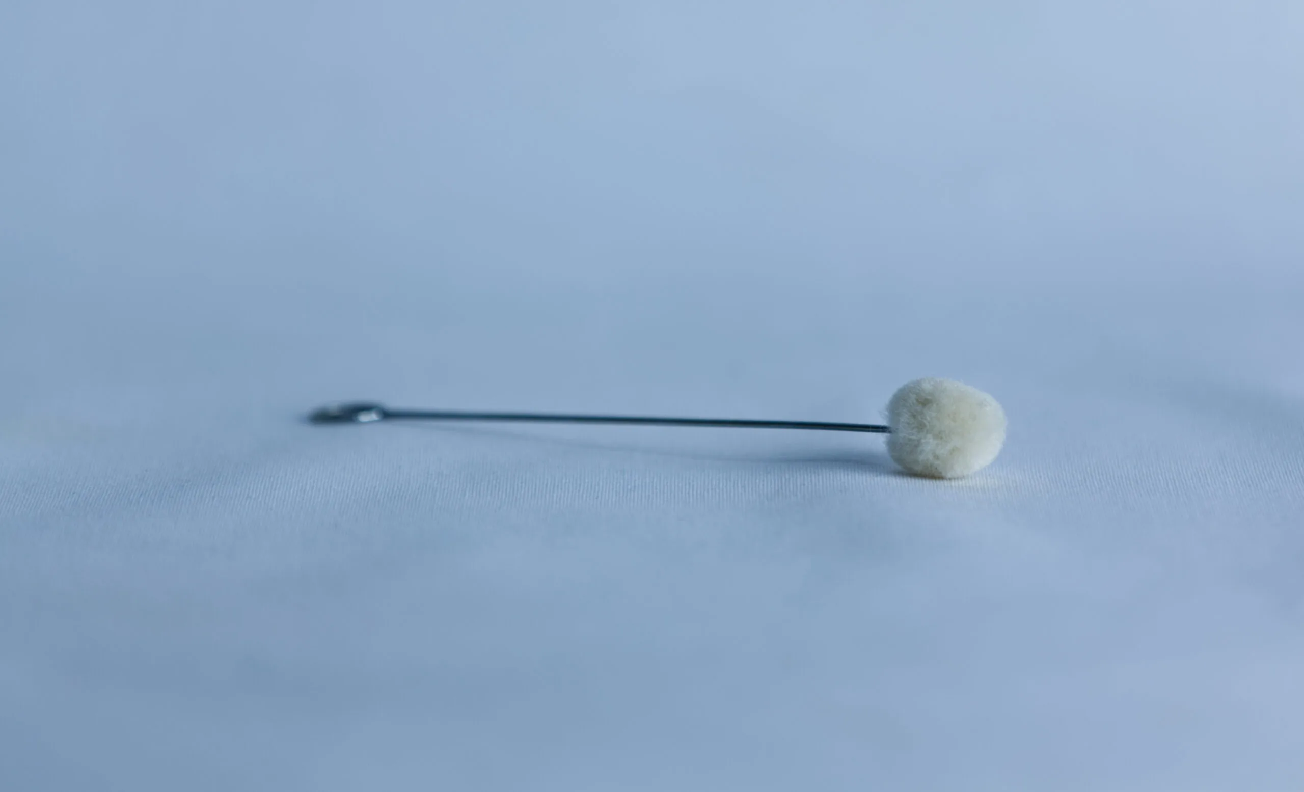 A single metal stick with a cotton bud lies on a smooth, light blue surface.