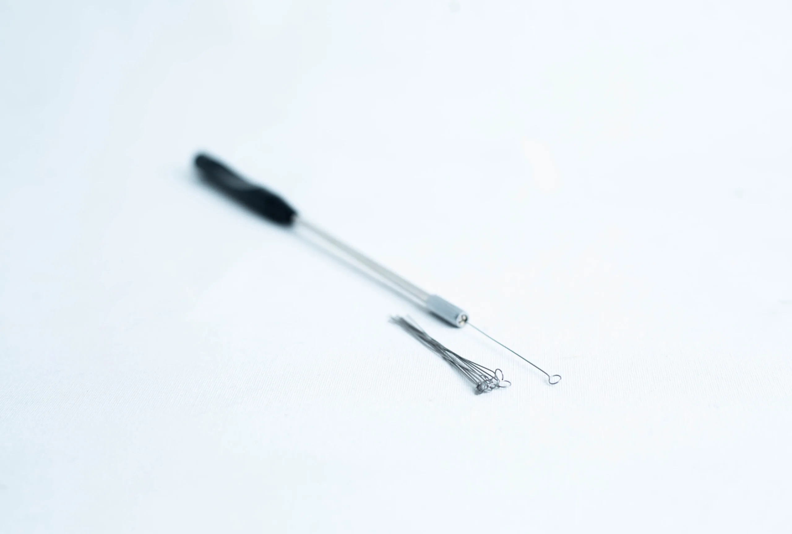 Close-up of a metal inoculating loop tool and spare loops on a white surface.