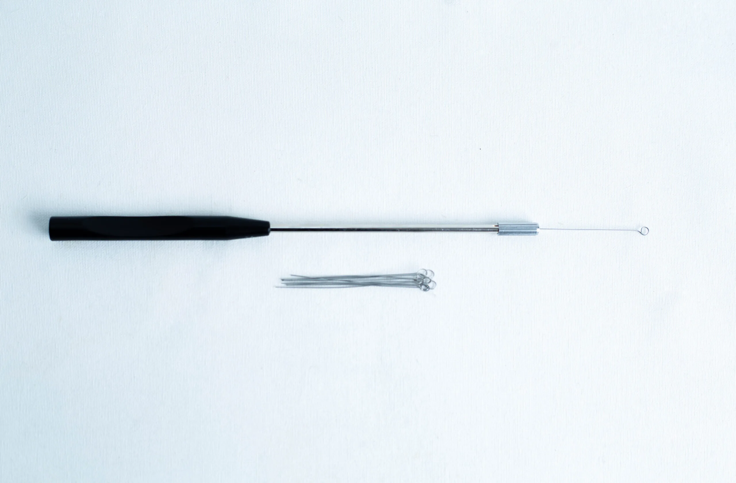 A black-handled inoculation loop and several metal loops on a white background.