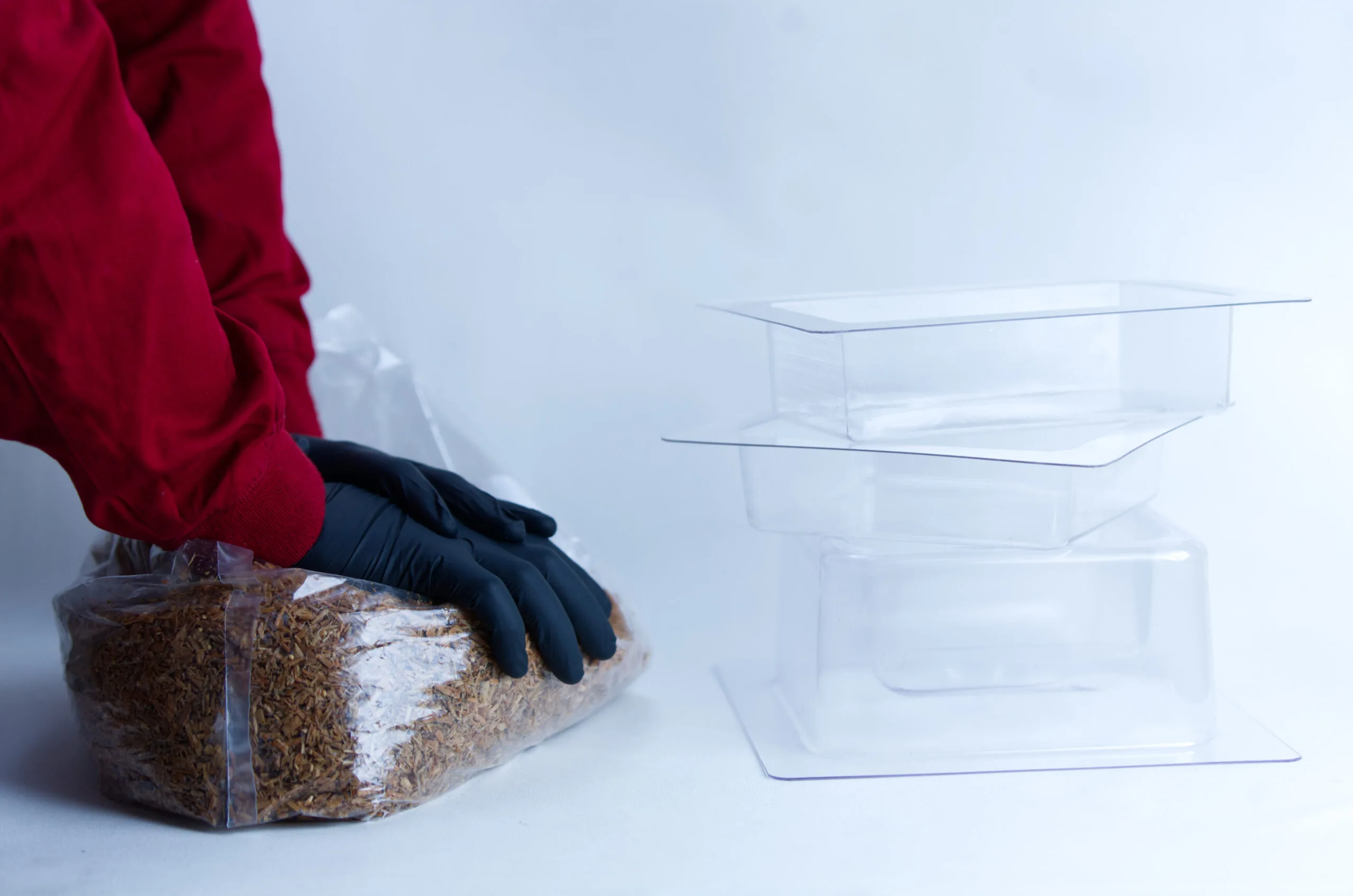 Person in red sleeves and black gloves handling a plastic bag of dried food beside empty plastic containers.