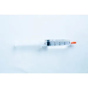 A plastic syringe with a red cap placed on a light blue surface.