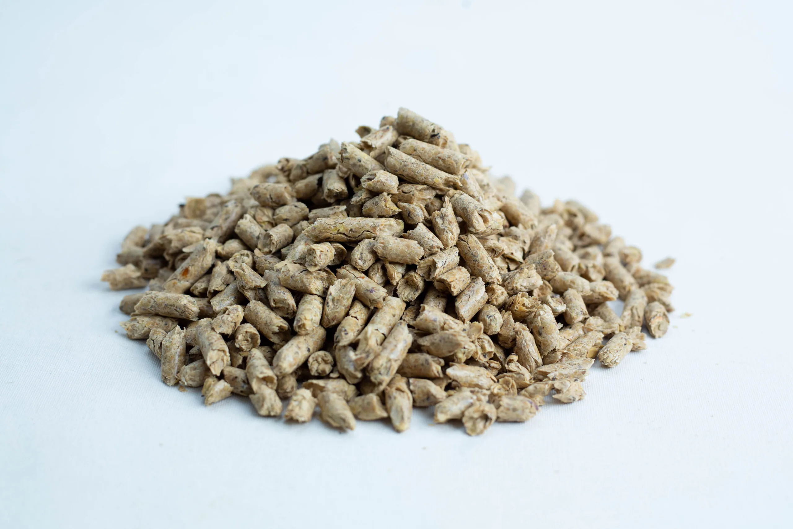 A pile of Maxisoy Soya Hull Pellets animal feed (20kg), light brown in colour, rests on a white background.