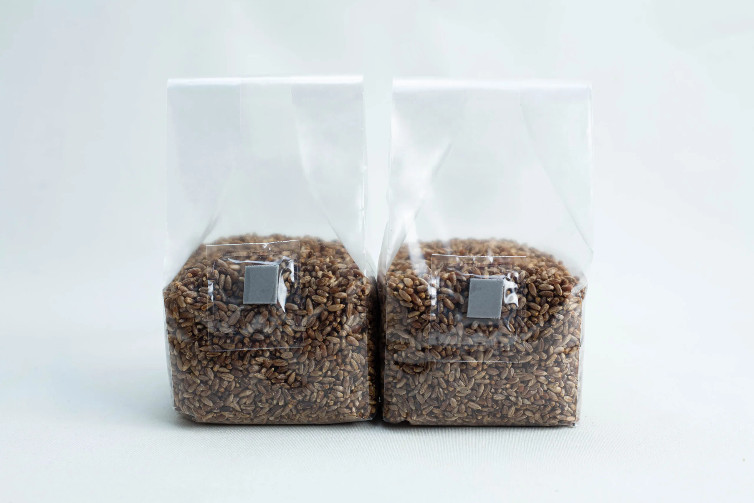 Two clear plastic bags filled with brown grains are placed side by side against a light background.