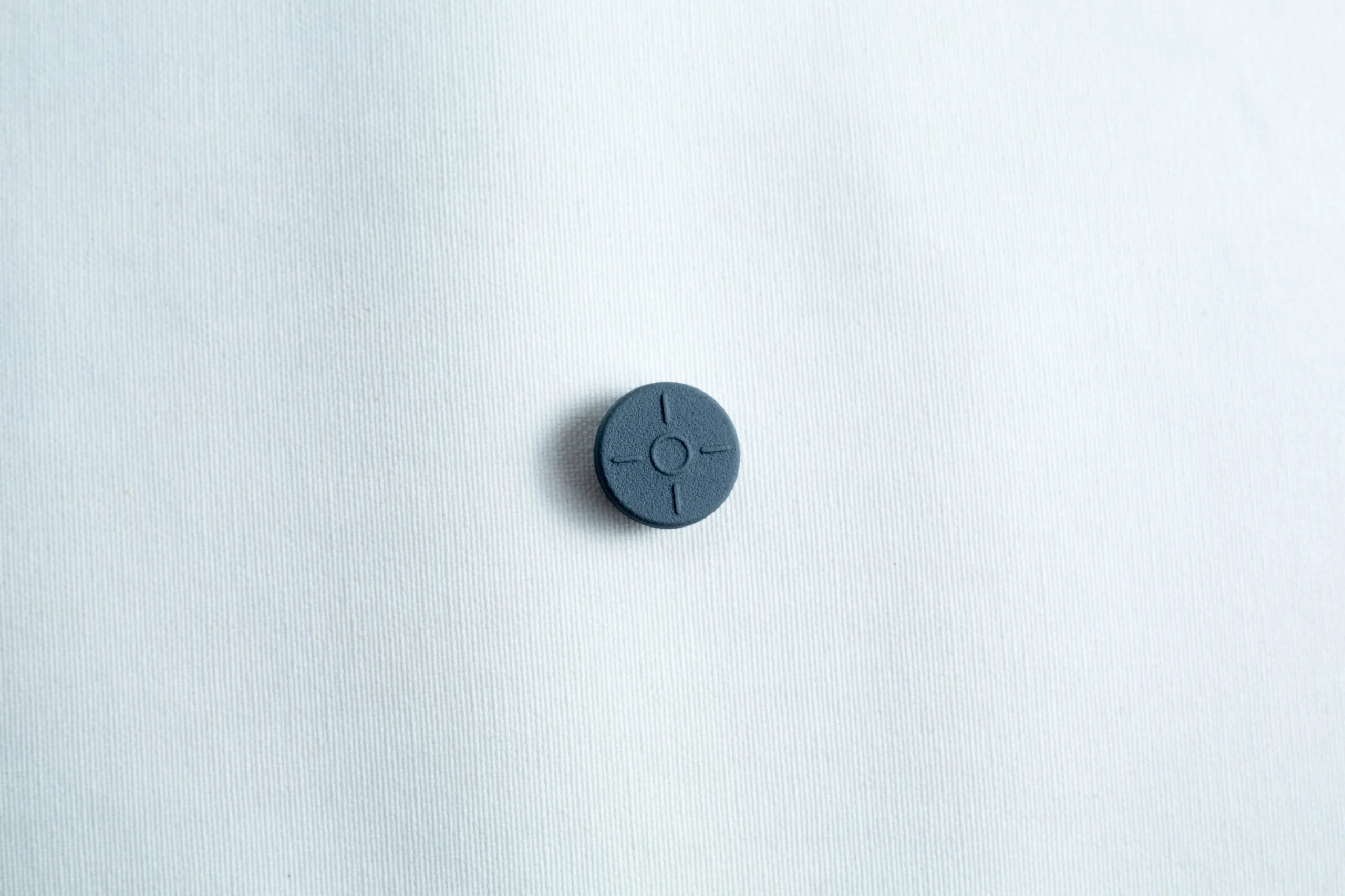 A single dark grey button with four holes on a plain white fabric background.