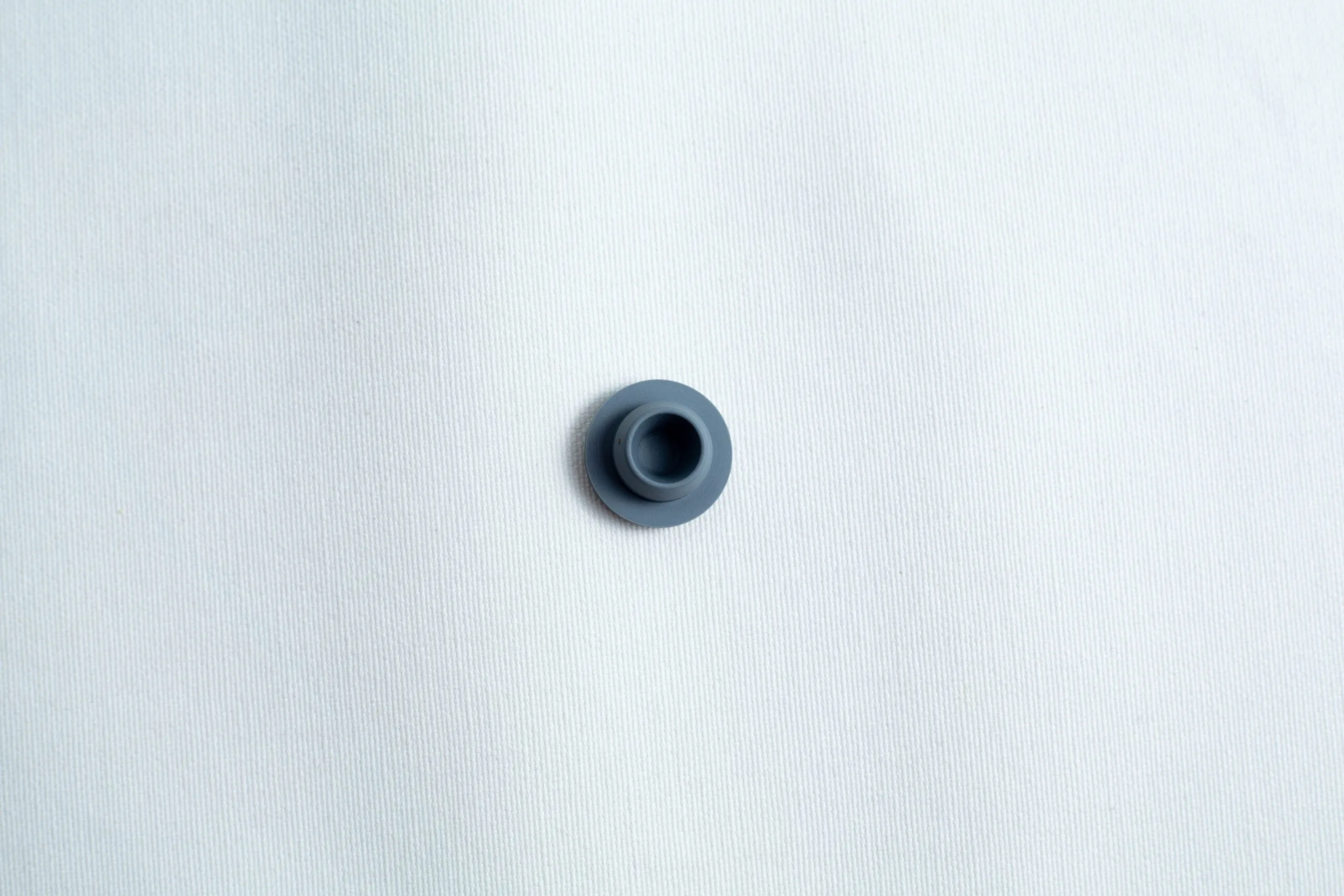 A single dark grey button on a plain white textured fabric background.