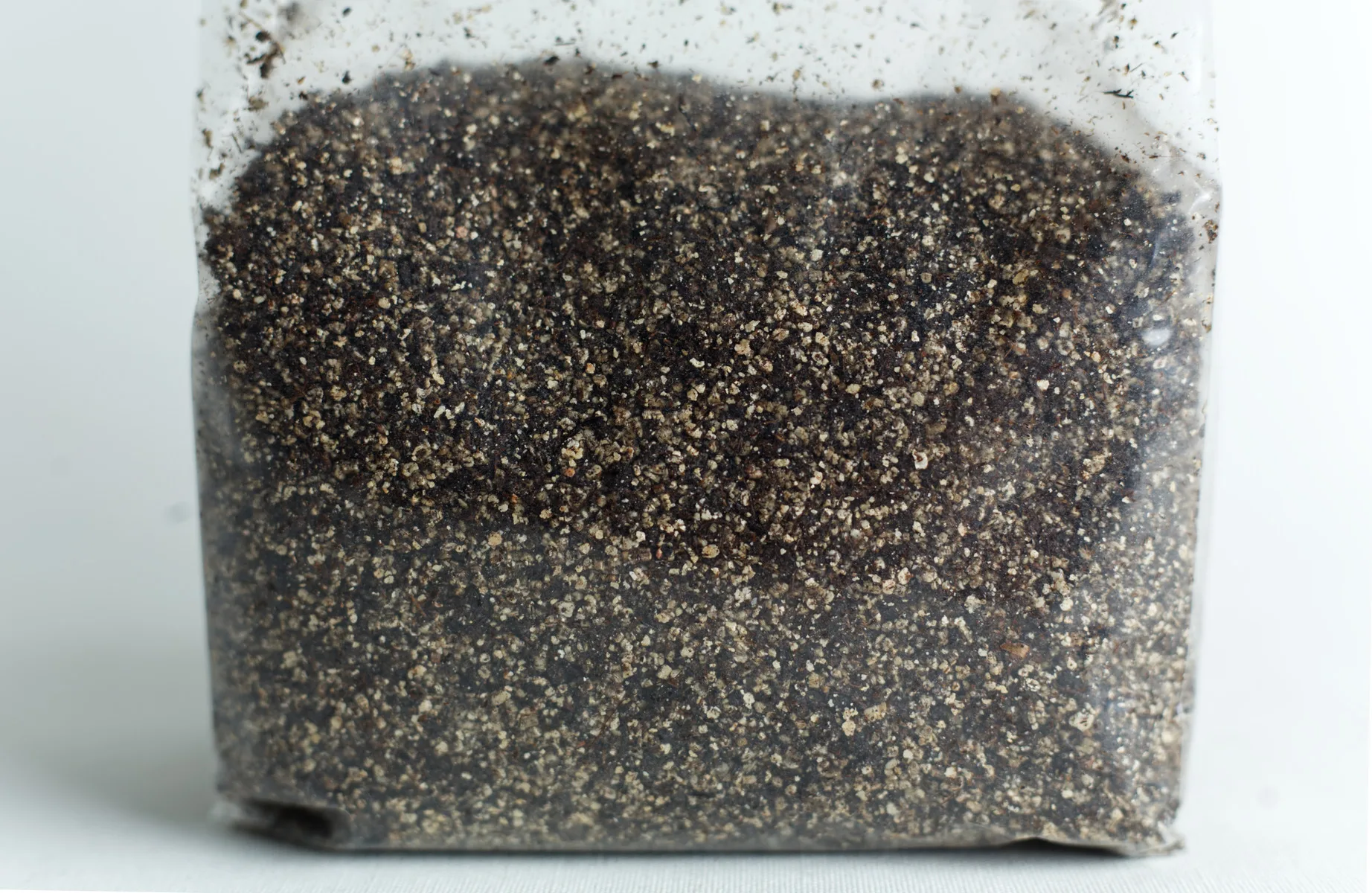 A clear plastic bag filled with coarse, dark soil or sand on a white surface.