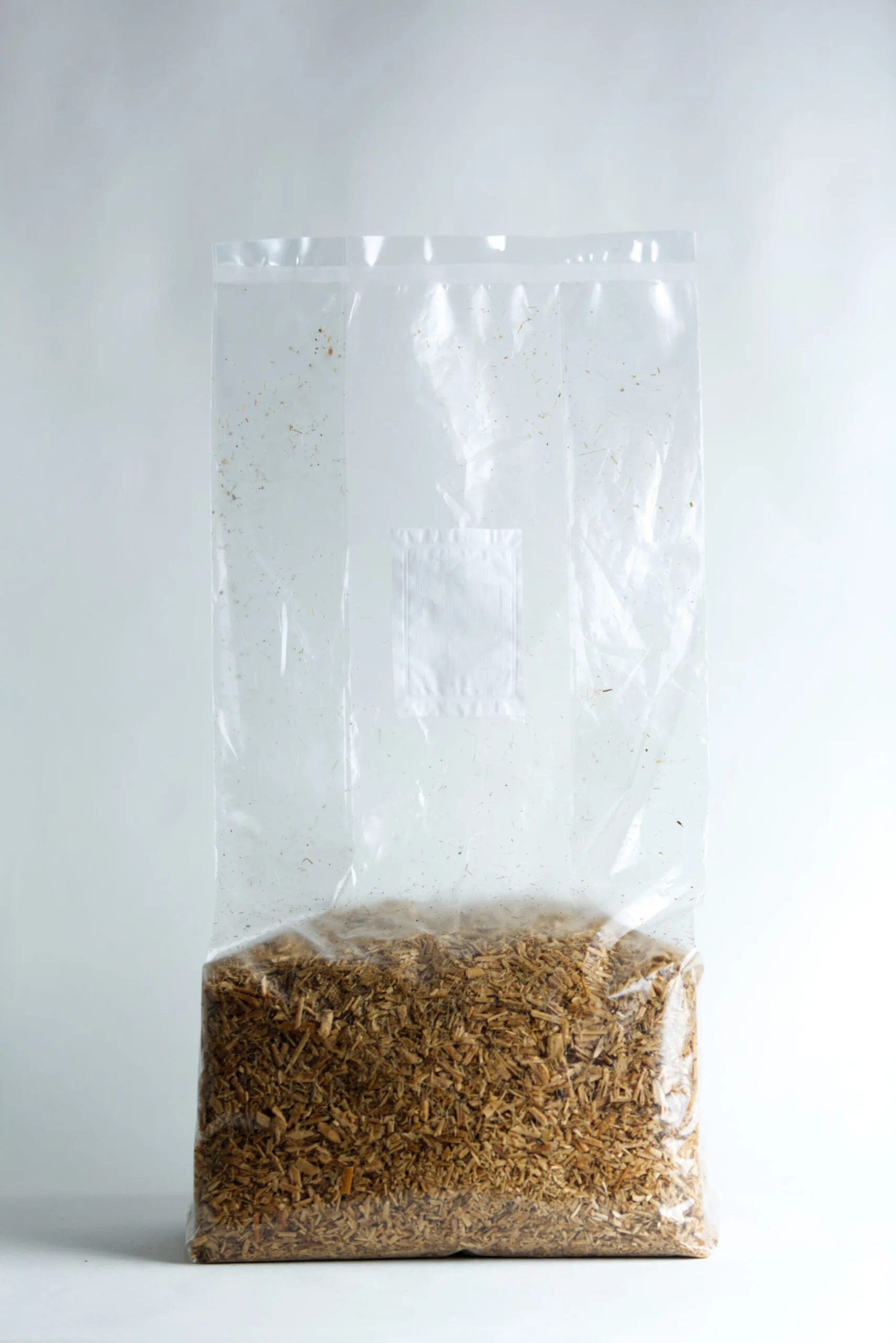 A clear plastic bag filled with brown woodchips against a plain white background.