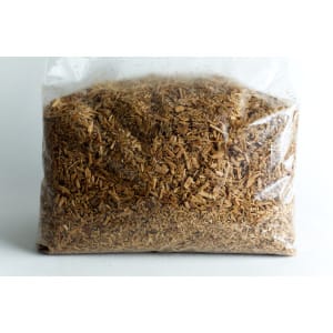 A clear plastic bag filled with chopped wood chips or shavings against a white background.