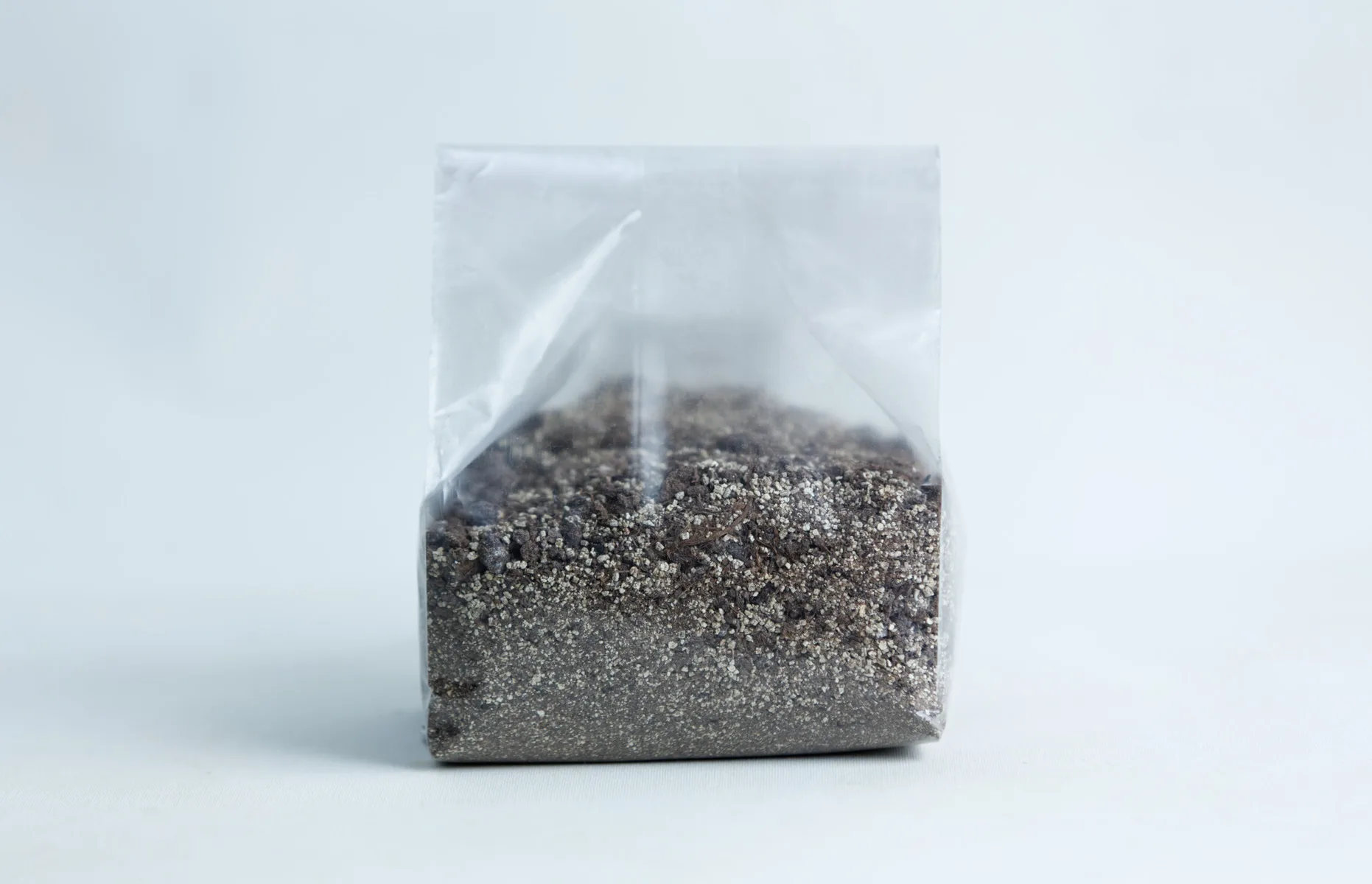 A clear plastic bag filled with sand and small pebbles, set against a plain white background.