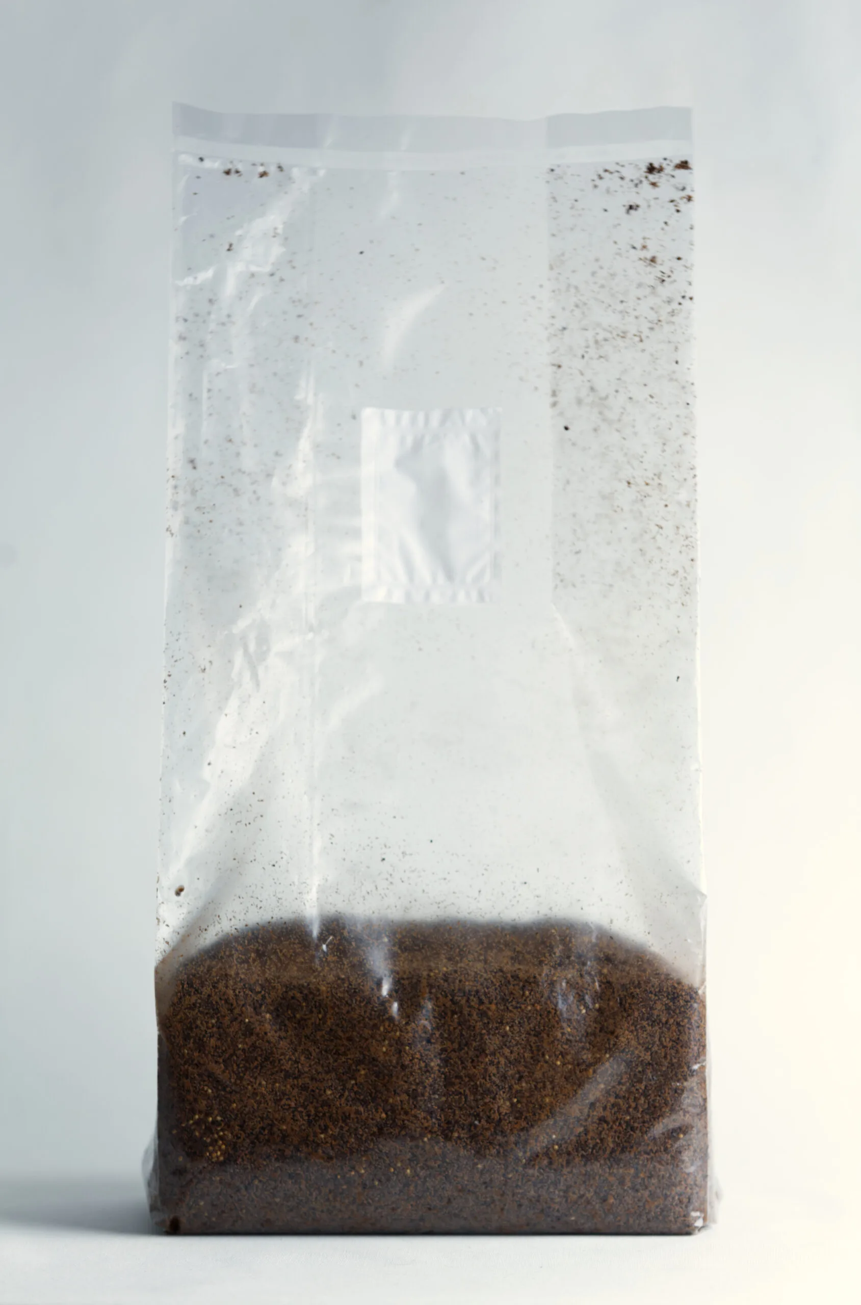 Clear plastic bag filled with brown coffee grounds against a plain background.