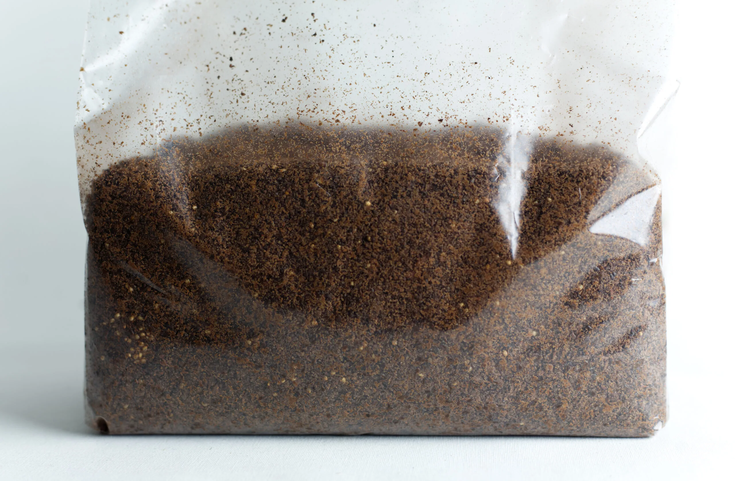 Clear plastic bag filled with brown ground coffee against a white background.
