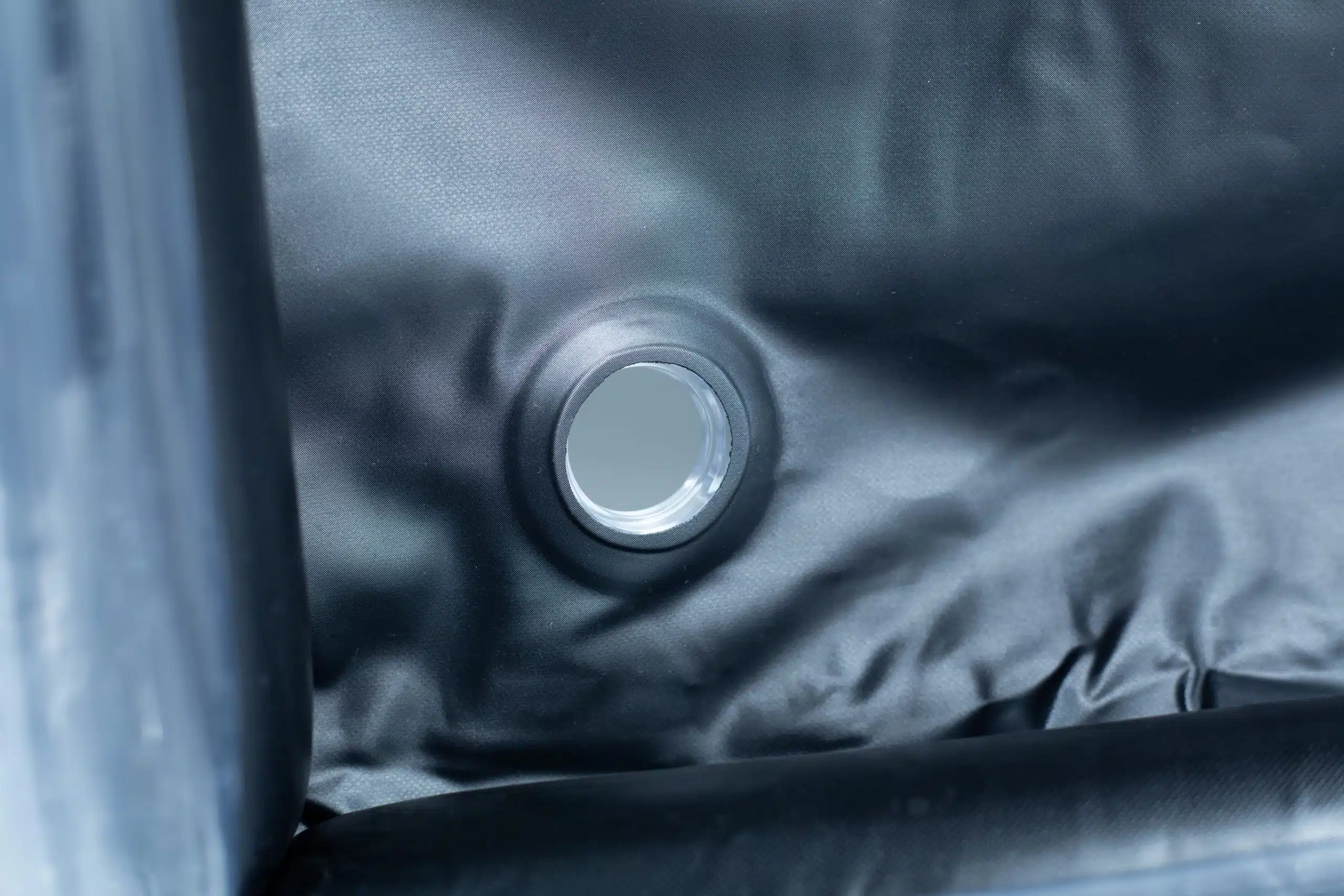Close-up of a circular metal drain hole in a dark, waterproof material, possibly an inflatable object.
