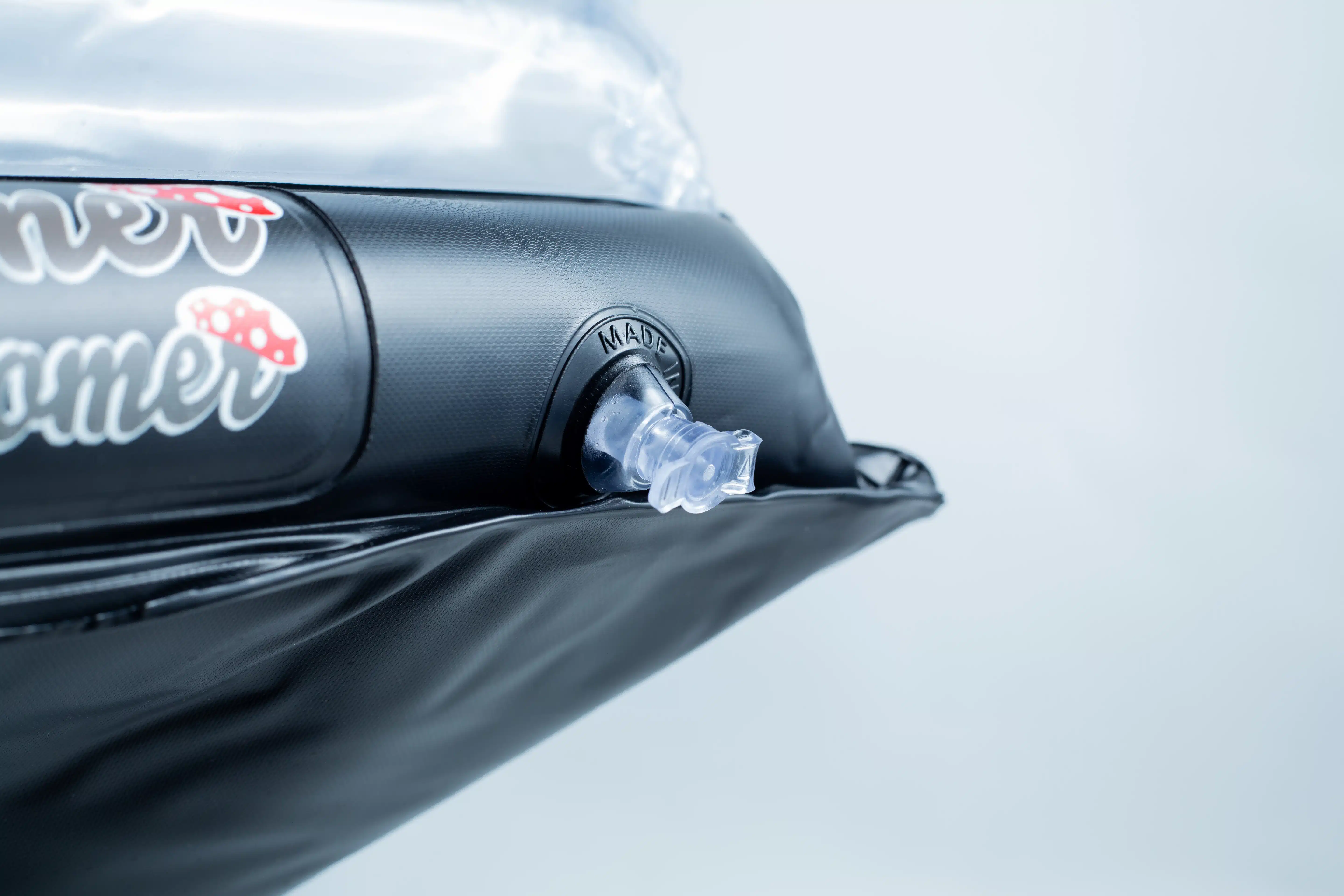 Close-up of an air valve on a black inflatable object with some stickers nearby.