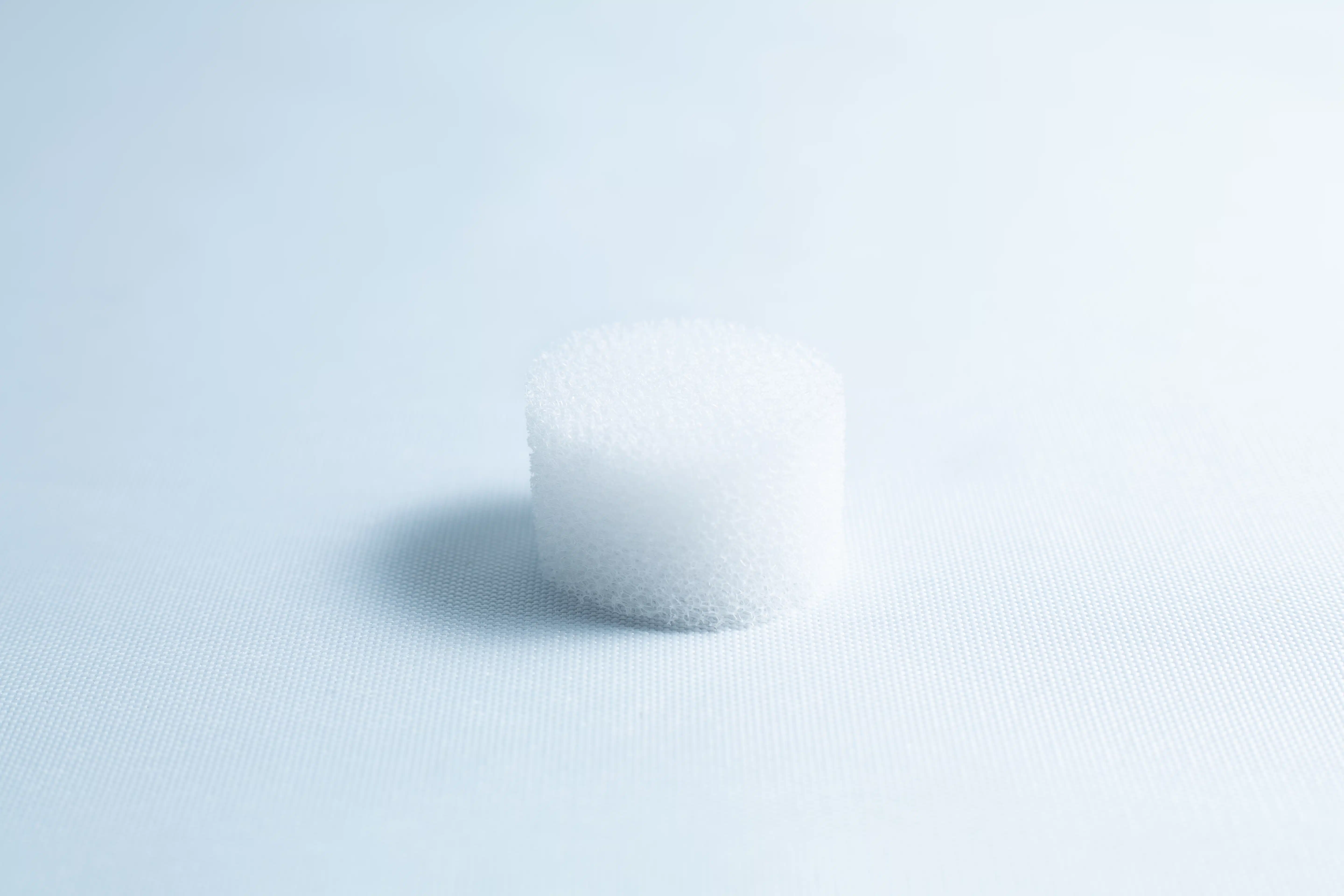 A small, white, cylindrical foam object sits on a light blue surface with soft lighting.
