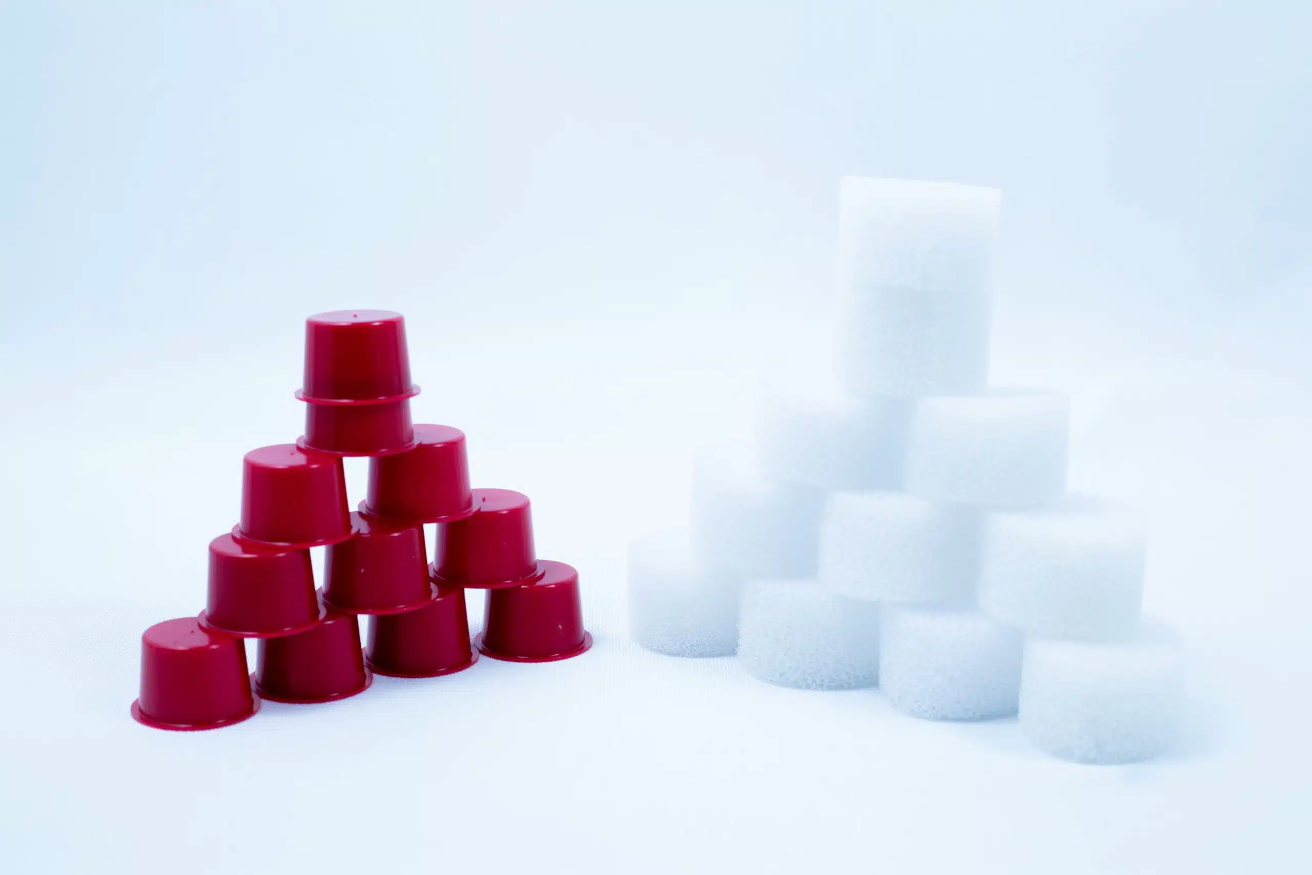 Red plastic cups and white cylindrical sponges are stacked in pyramid shapes on a white background.