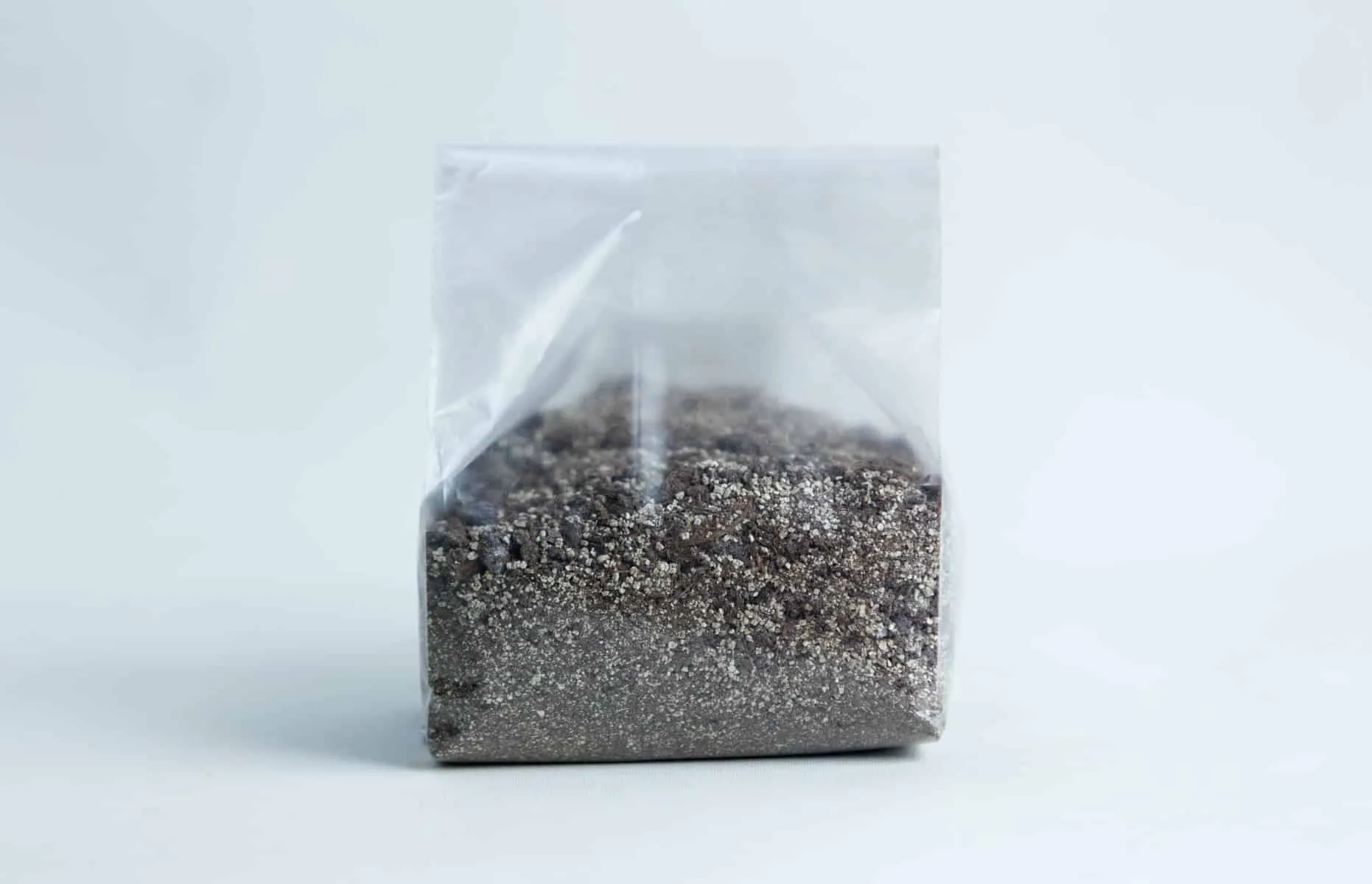 Monotub Mushroom Growing Kit-Premium 8 A clear plastic bag filled with a mixture of small, dark and light grainsโperfect for use with the Monotub Mushroom Growing Kit-Premiumโset against a plain background.