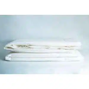 Two neatly folded white bed sheets rest on a light surface with a soft blue backdrop, making them an ideal match for the Light Log Blanket.