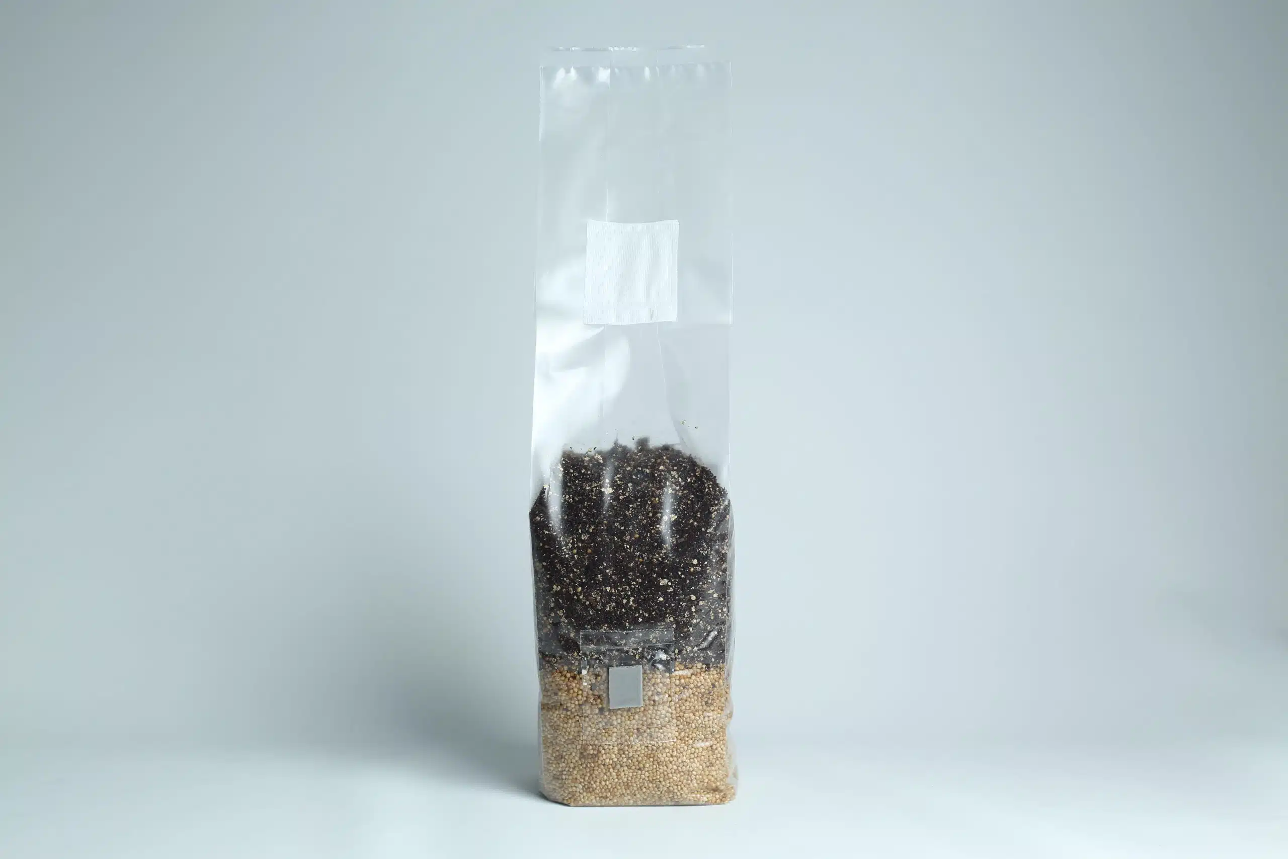 Manure Based All in One Mushroom Grow Bag |1kg 2 Clear plastic bag filled halfway with mixed grains and seeds, standing upright on a plain background.