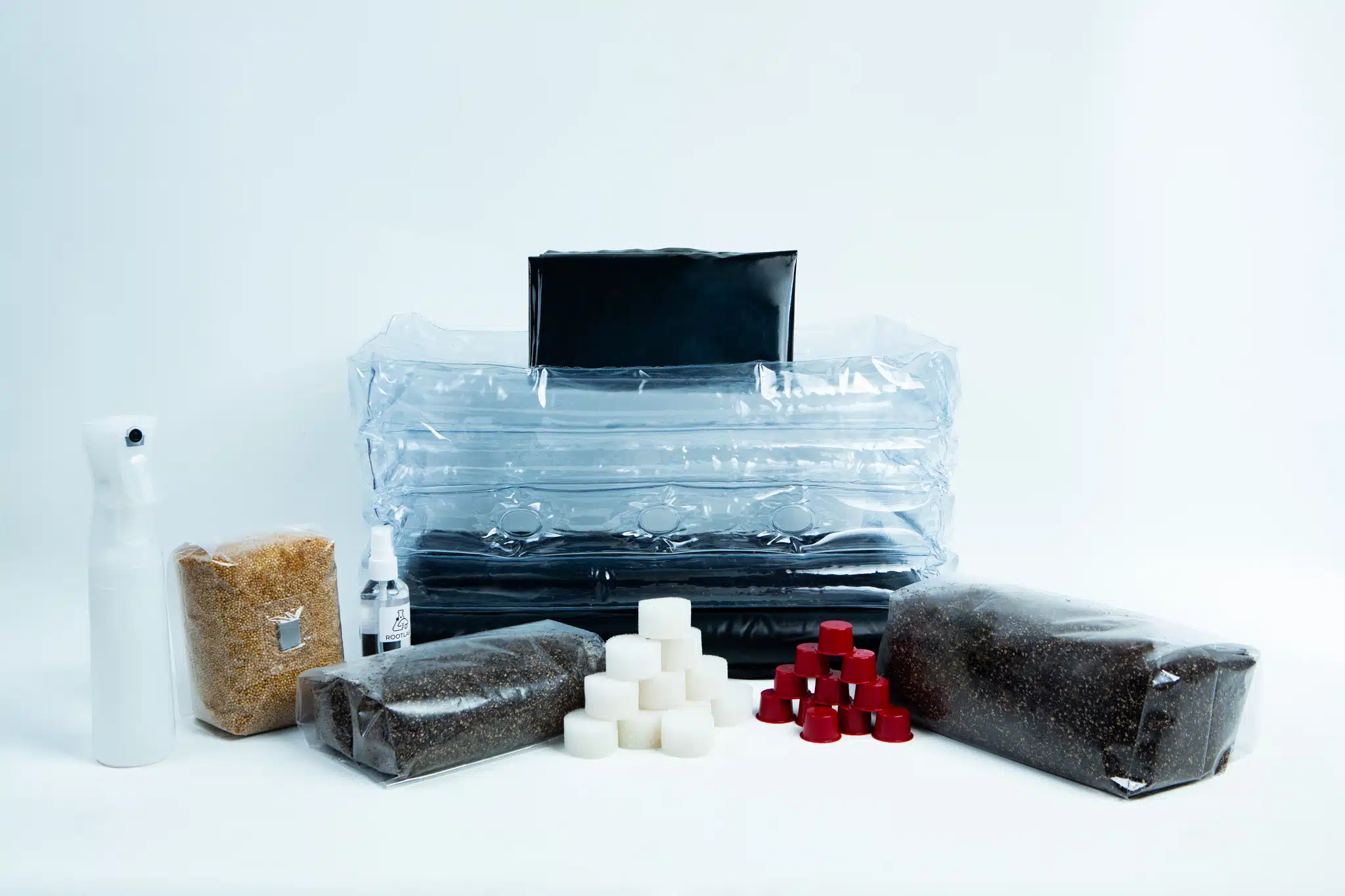 Monotub Mushroom Growing Kit-Premium 2 A mushroom growing kit with bags of substrate, a spray bottle, and small cubes on a white background.